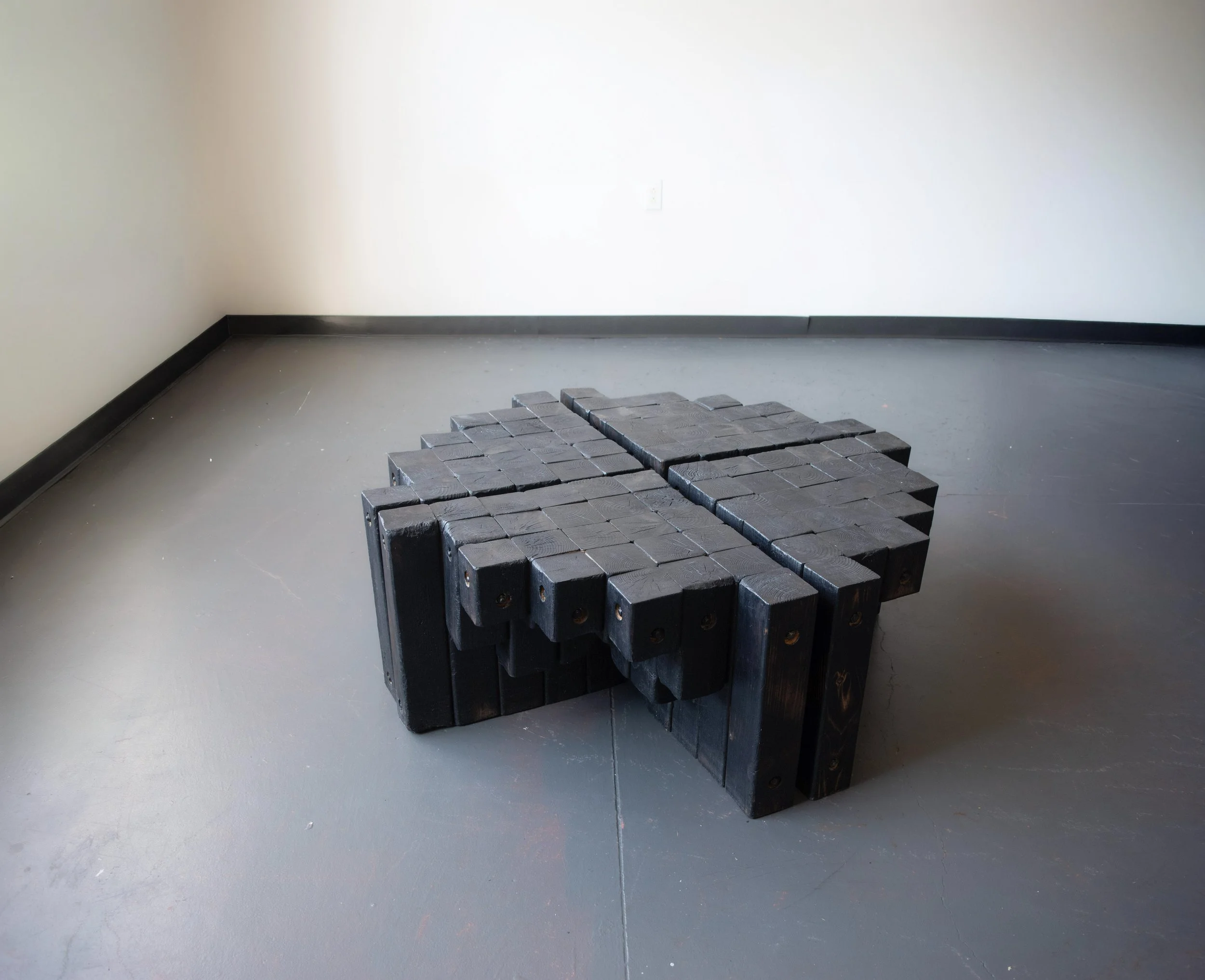 Empty room with white walls, black baseboards, gray floor, and stacked black metal blocks in the foreground.