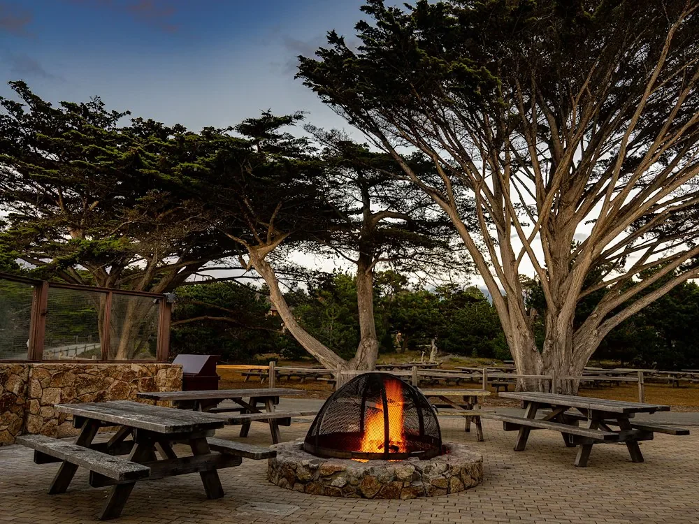 a-peaceful-outdoor-area-with-wooden-picnic-tables-surrounds-a-lit-fire-pit-asilomar-hotel-and-conference-grounds-pacific-grove-california.webp