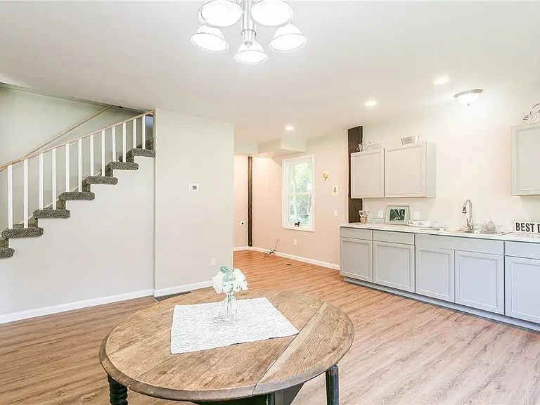 Open-concept living space with a dining table, staircase, and kitchen area featuring gray cabinets and a window.
