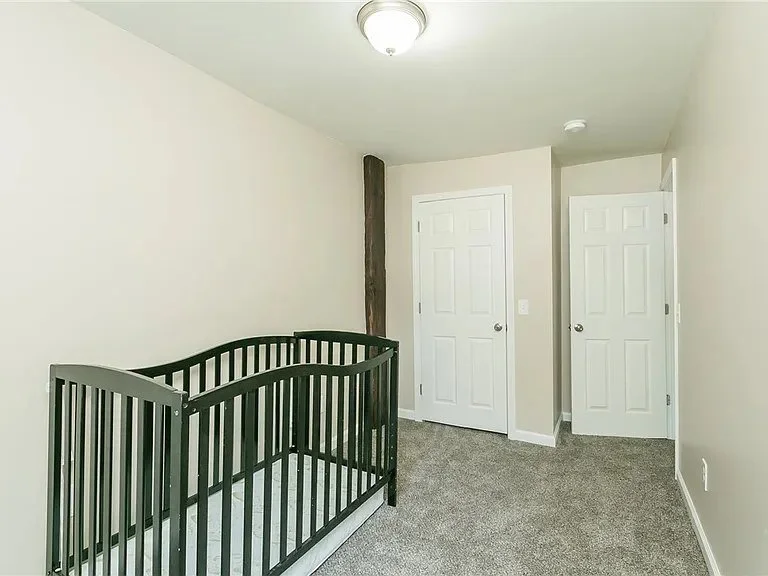 Empty bedroom with a black crib, closed white doors, beige walls, and gray carpet.