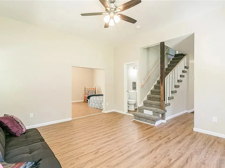 Living room with hardwood floors, ceiling fan, stairs leading to upper floor, small bathroom, and an opening to a bedroom.