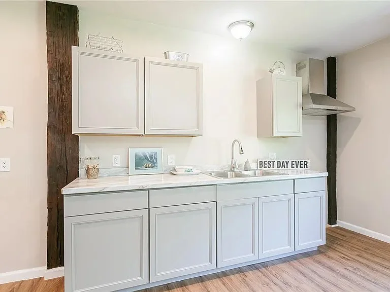 Simple white kitchen with upper and lower cabinets, a marble countertop, a sink, and drawers, with a sign saying 'Best Day Ever' on the counter.