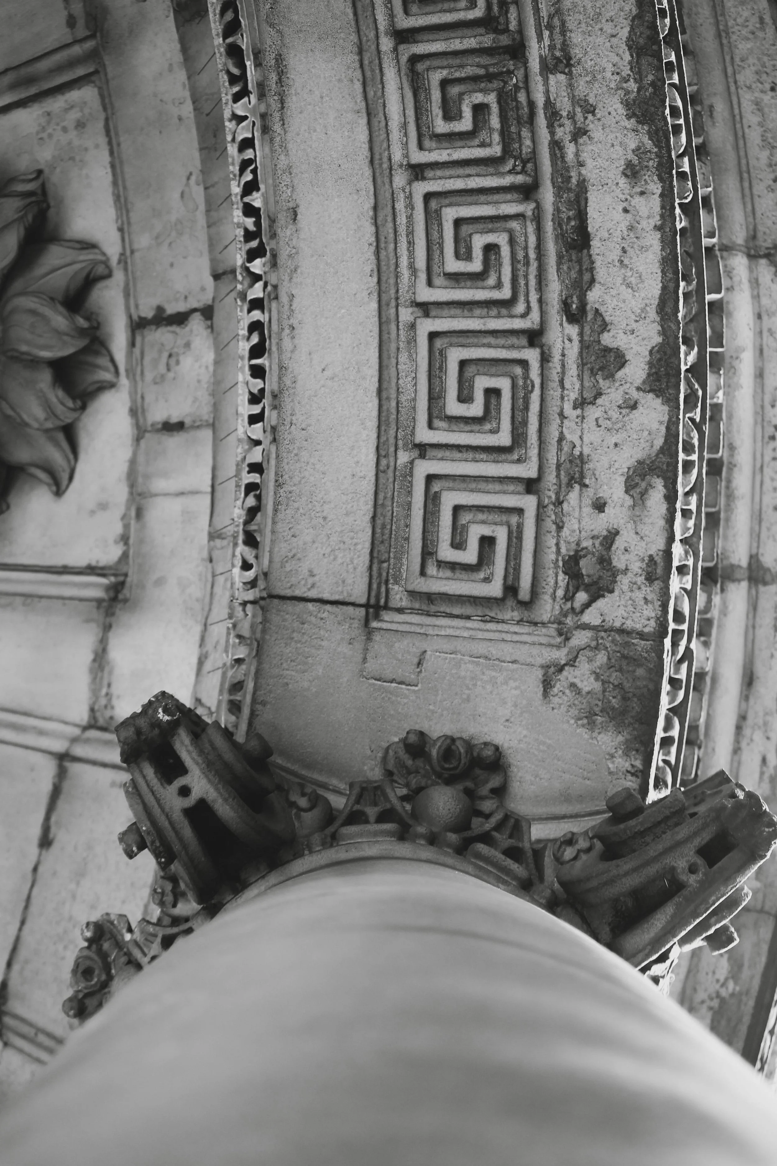 Close-up of intricate Greek key patterned decorative concrete or stonework with tools and fallen leaves nearby.