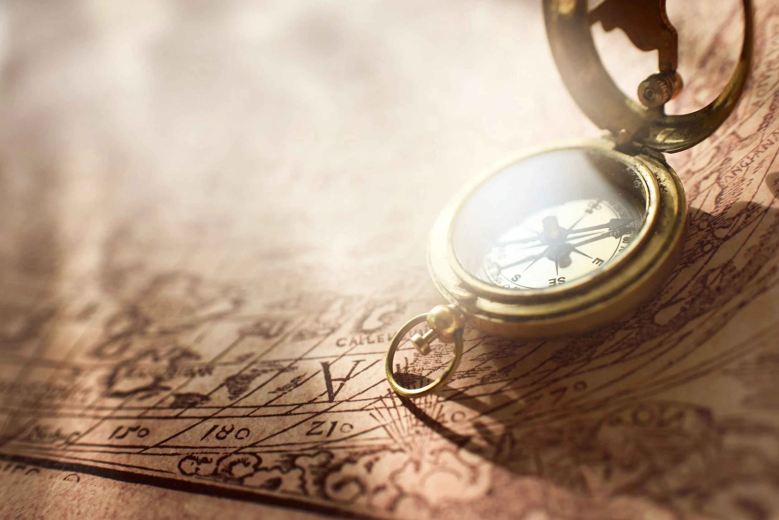 A vintage brass compass placed on an old detailed map with geographic markings and place names.