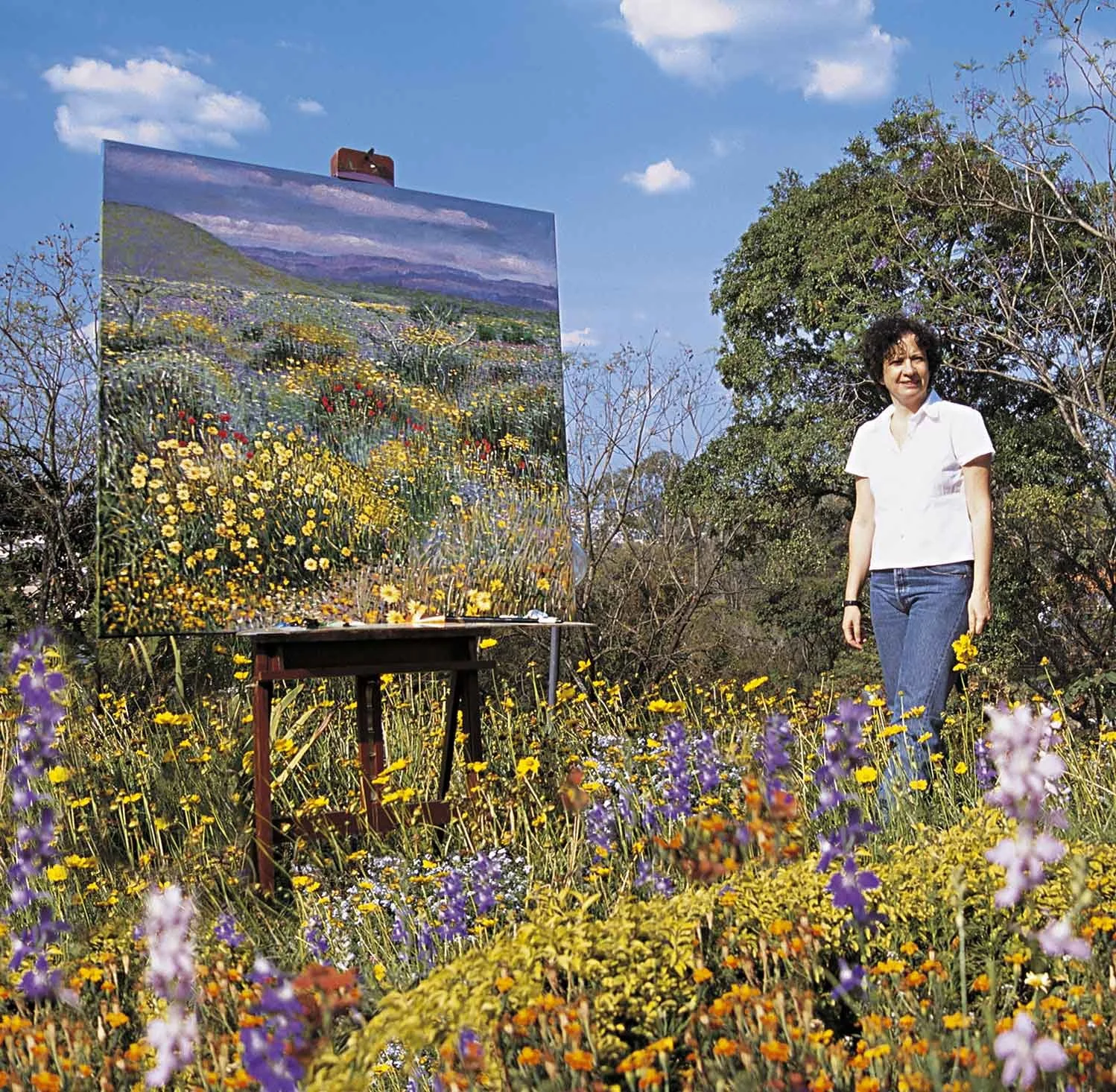 Mulher em campo de flores com pintura ao ar livre de uma paisagem de flores e montanhas ao fundo