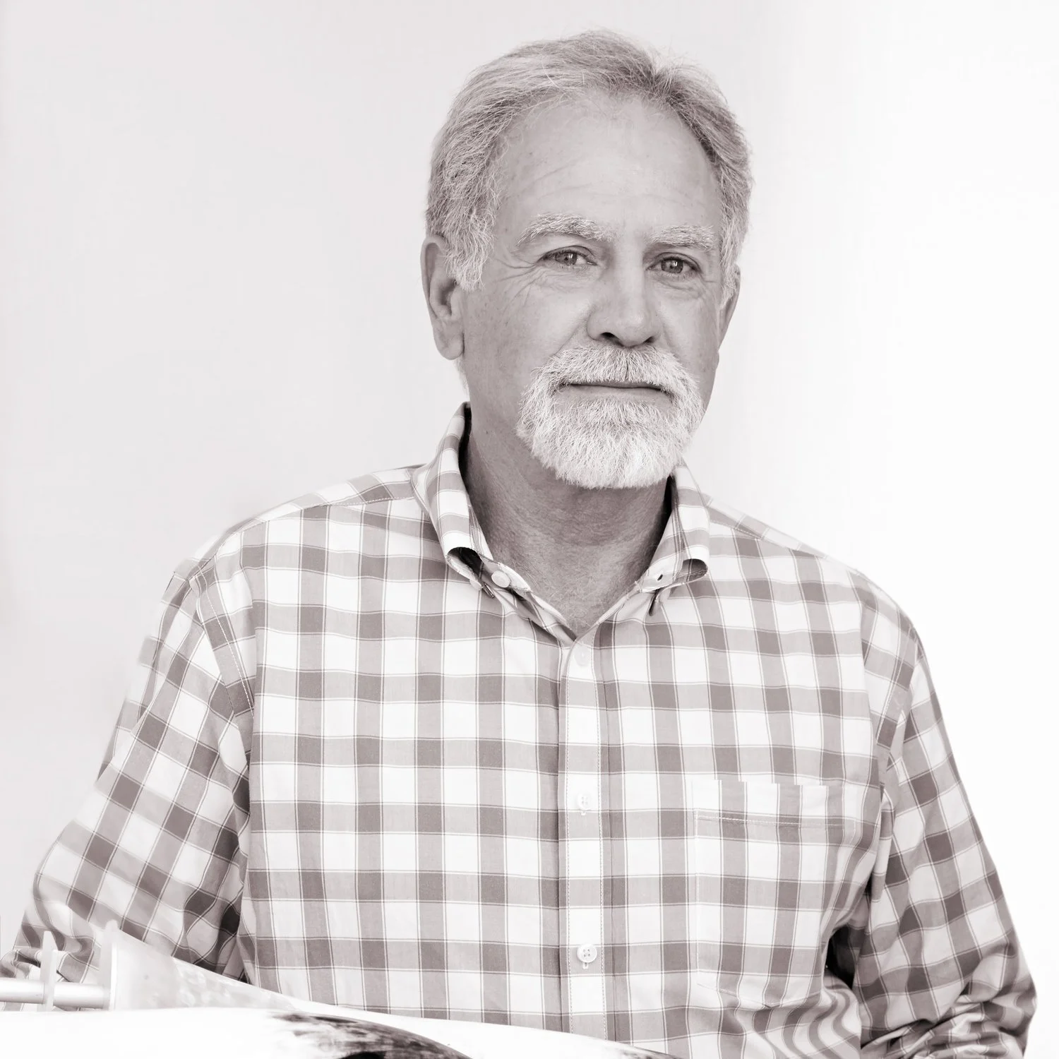 A black and white portrait of an older man with a white beard and mustache, wearing a plaid button-up shirt, looking at the camera with a neutral expression.