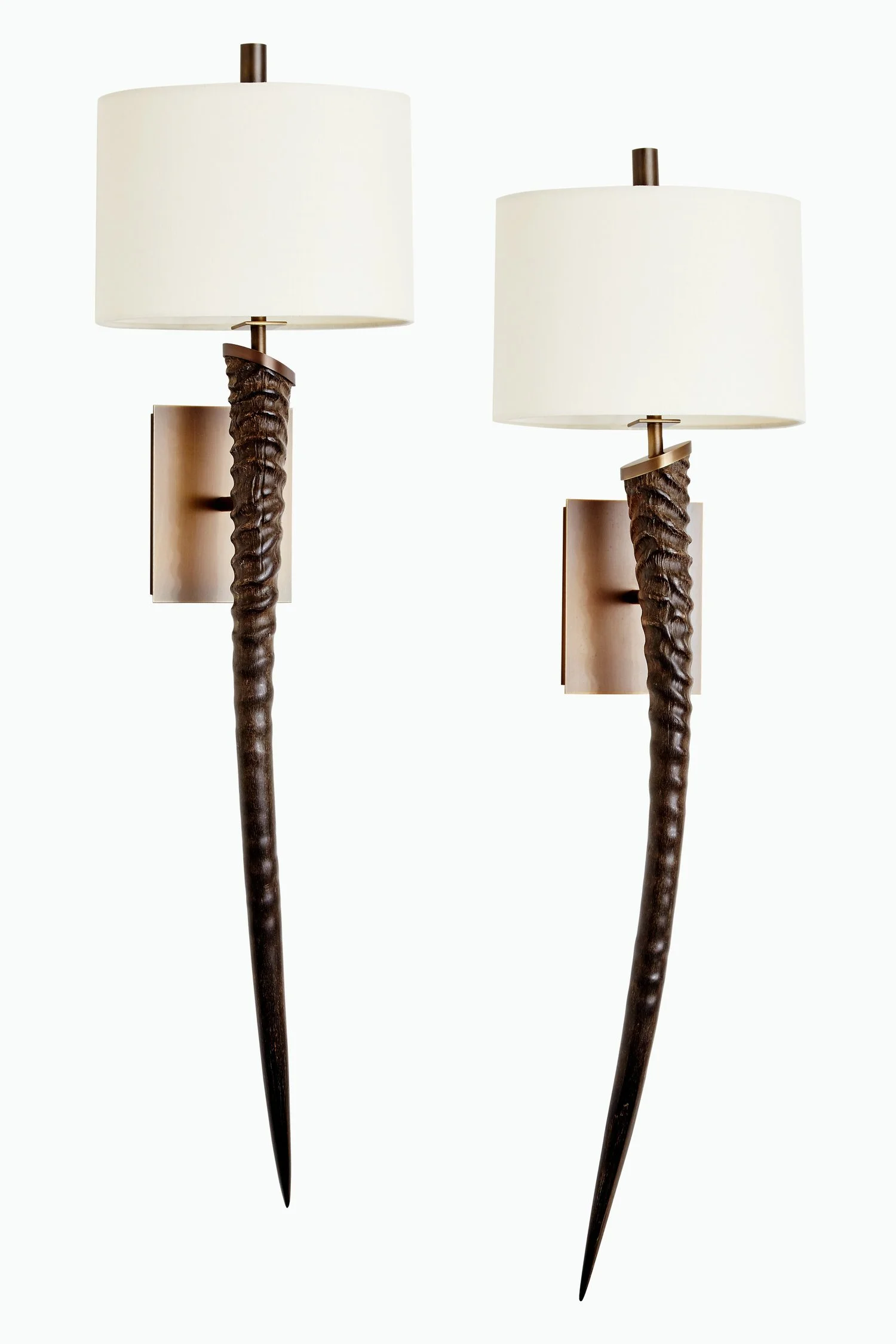 Two wall-mounted lamps with white cylindrical shades, dark textured vertical bases, and pointed black tips, set against a plain background.