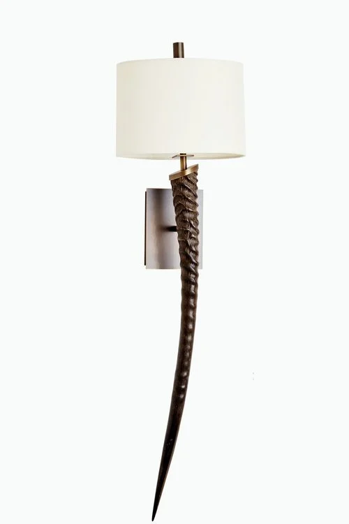 Wall-mounted lamp with a white lampshade and a dark, curved, textured base resembling animal tusk or horn.
