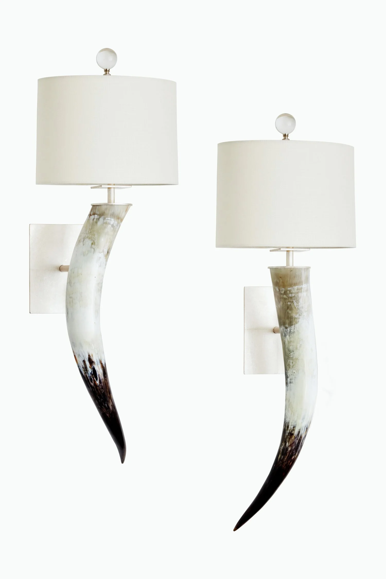 Two modern table lamps with curved, ivory-colored bases made of horn or marble, mounted on rectangular backplates, with large cylindrical white fabric lampshades and spherical finials on top, set against a plain white background.