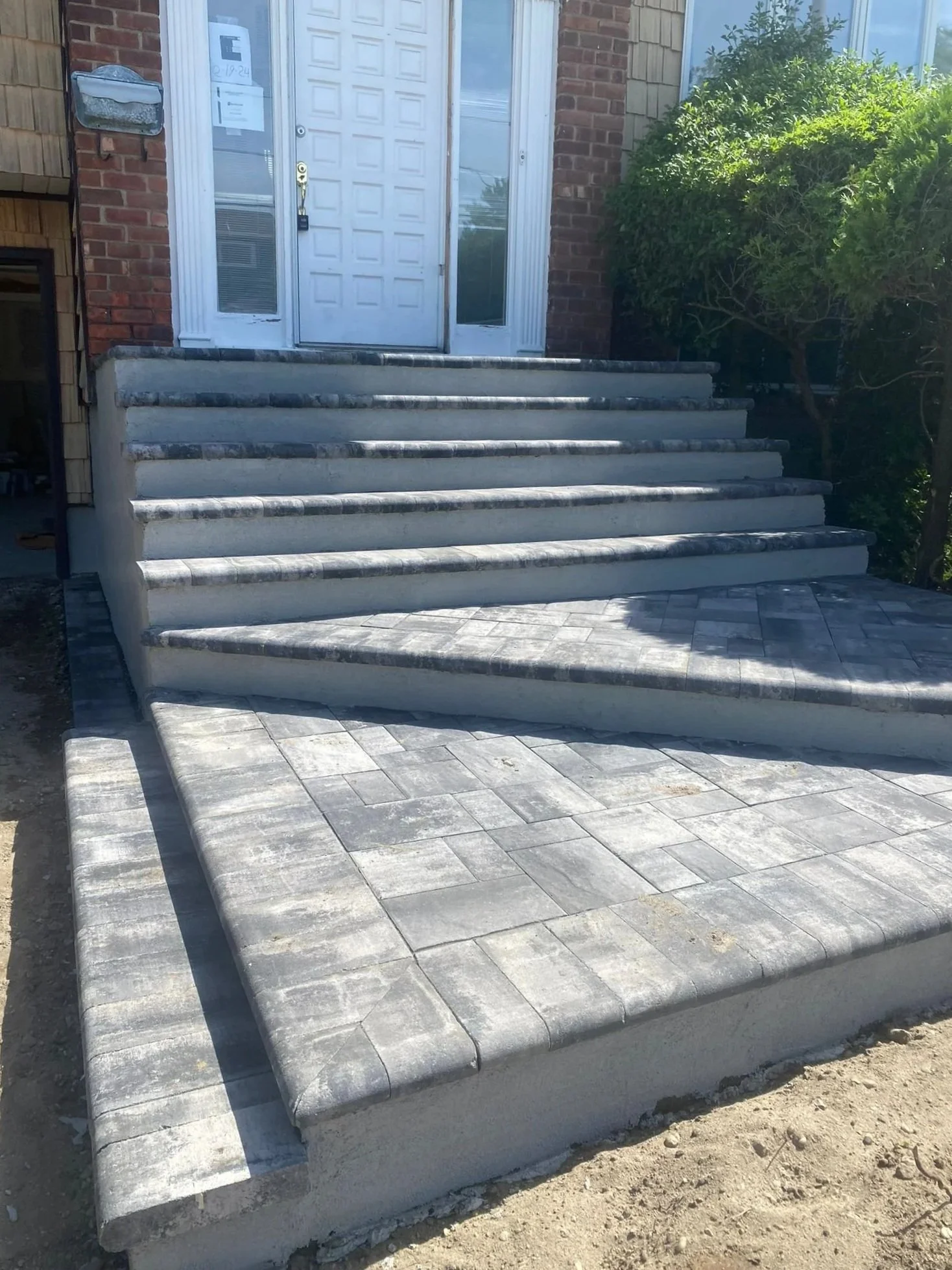 A set of concrete stairs leading up to a white front door of a house, with a bush on the right side and a brick and siding exterior.