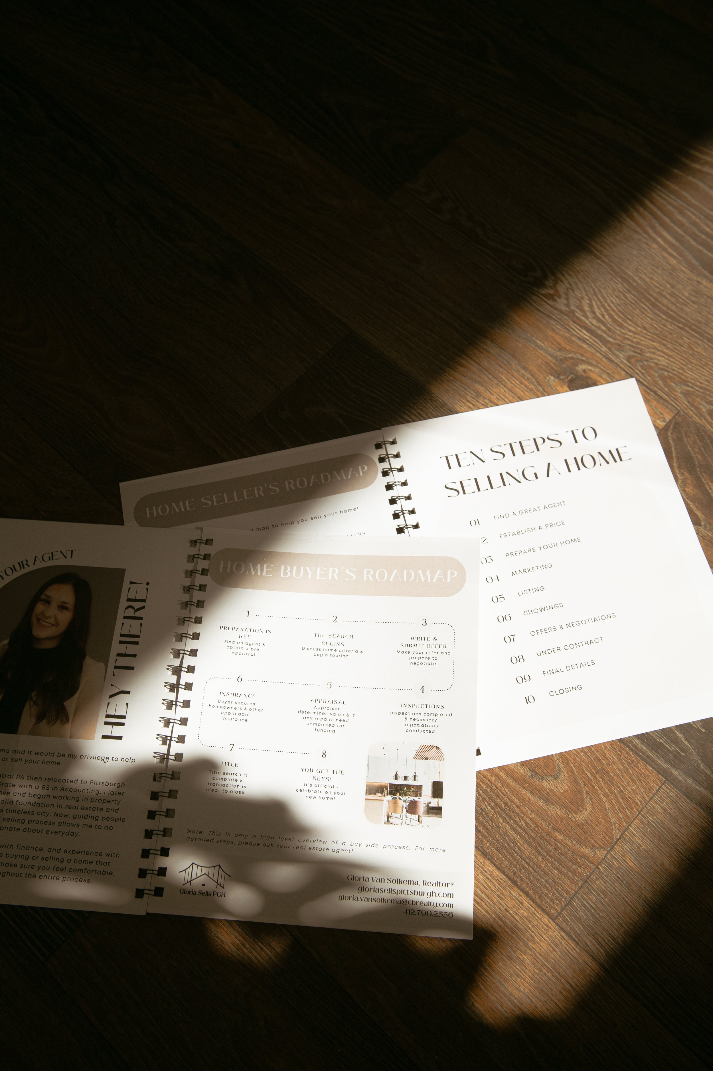 Open book or brochure on a dark wooden surface with visible grain pattern, displaying pages titled 'Home Seller's Roadmap' and 'Home Buyer's Roadmap' with numbered steps and a small photograph of a woman.