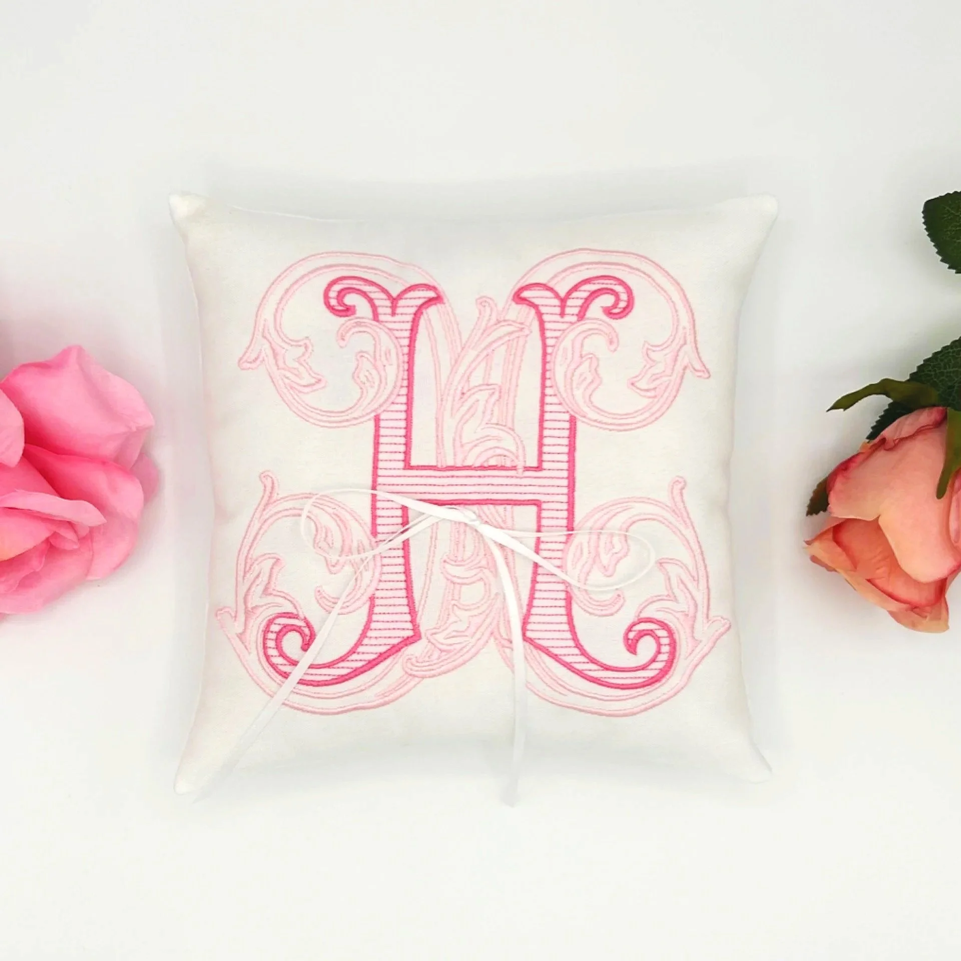 Close-up of an embroidered design on a white fabric pillow, featuring pink thread forming intricate patterns with a symmetrical motif.
