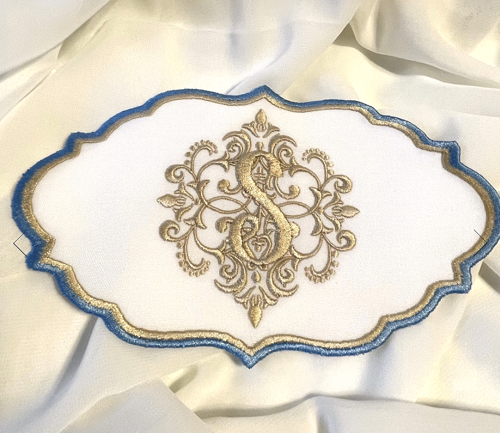 Decorative embroidered cloth with gold and blue details and a central design featuring a seahorse, floral elements, and a heart.