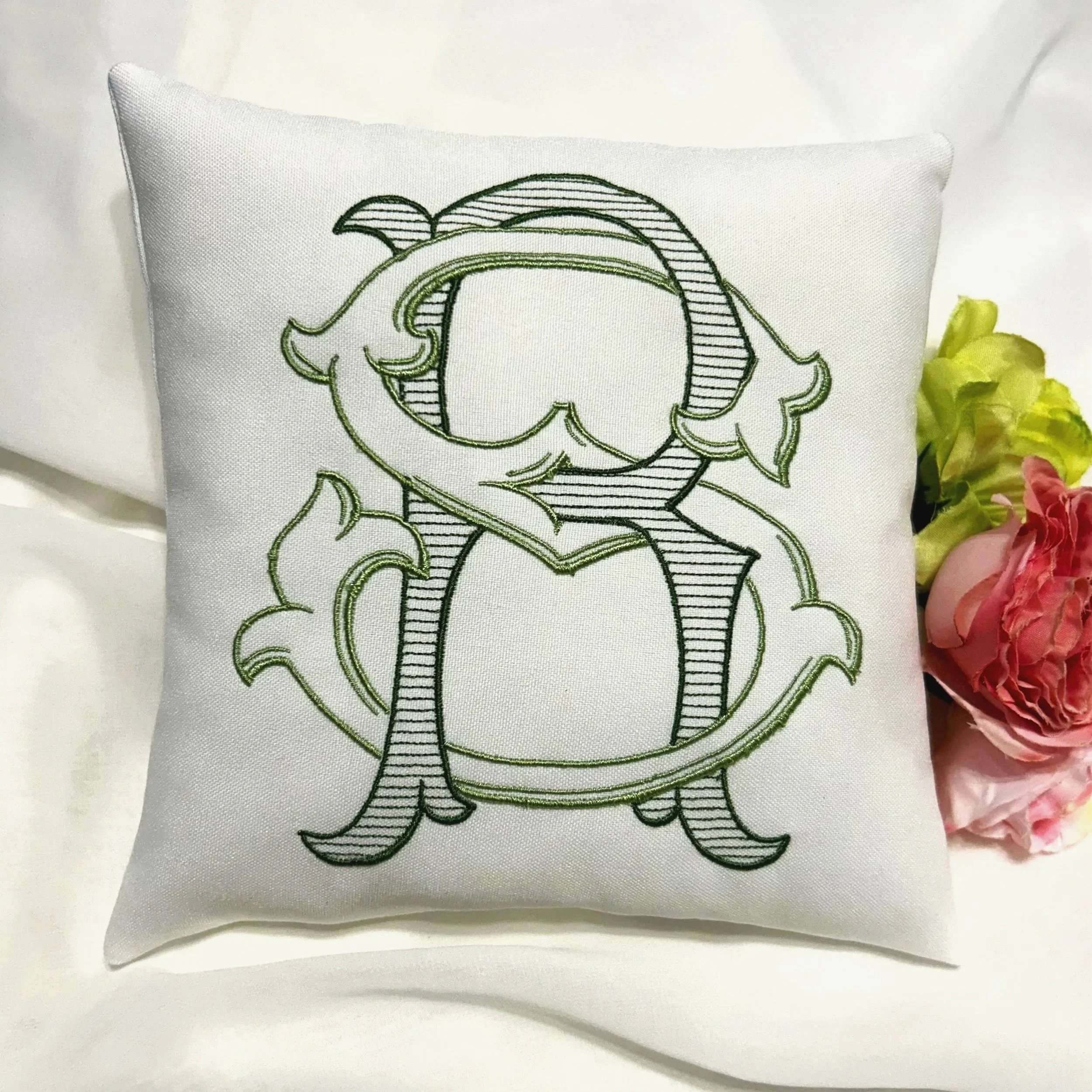 White pillow with green embroidered elephant outline on fabric, positioned to the left of pink and yellow flowers.