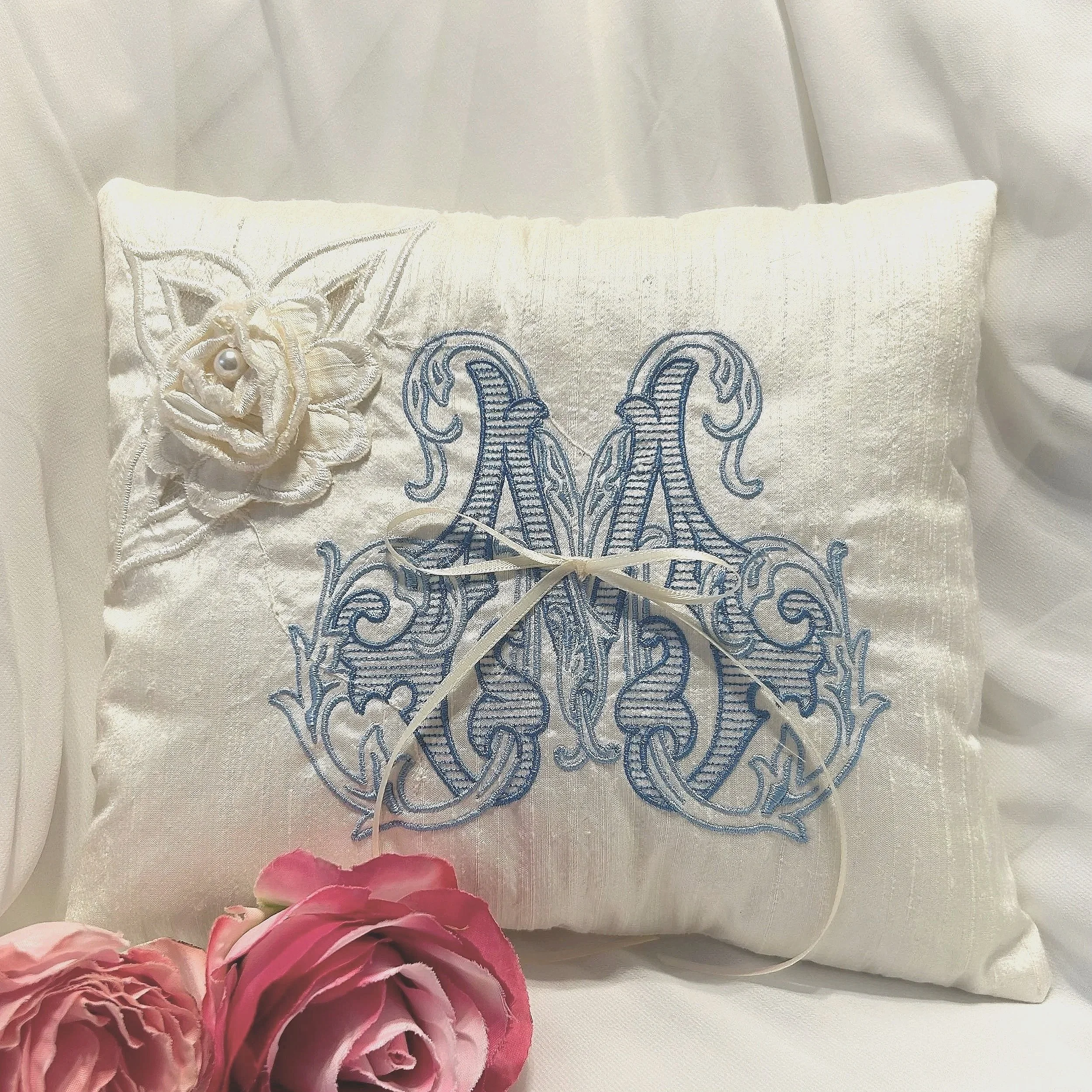 Close-up of a white embroidered cloth with floral details and a blue embroidered design, accompanied by pink and red flowers at the bottom.
