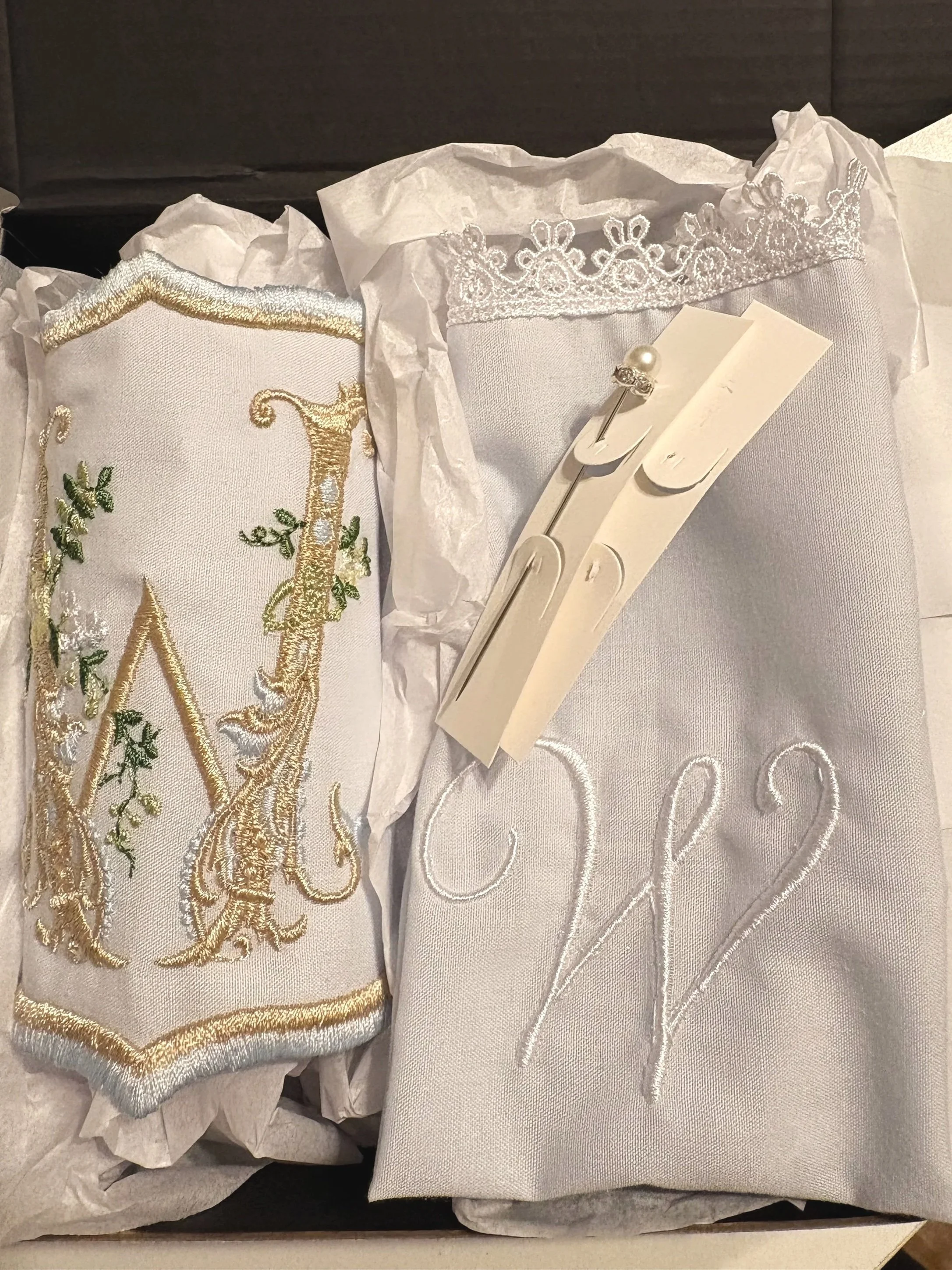A decorative pillow with gold embroidery and a white embroidered fabric with lace trim and a pearl-headed pin