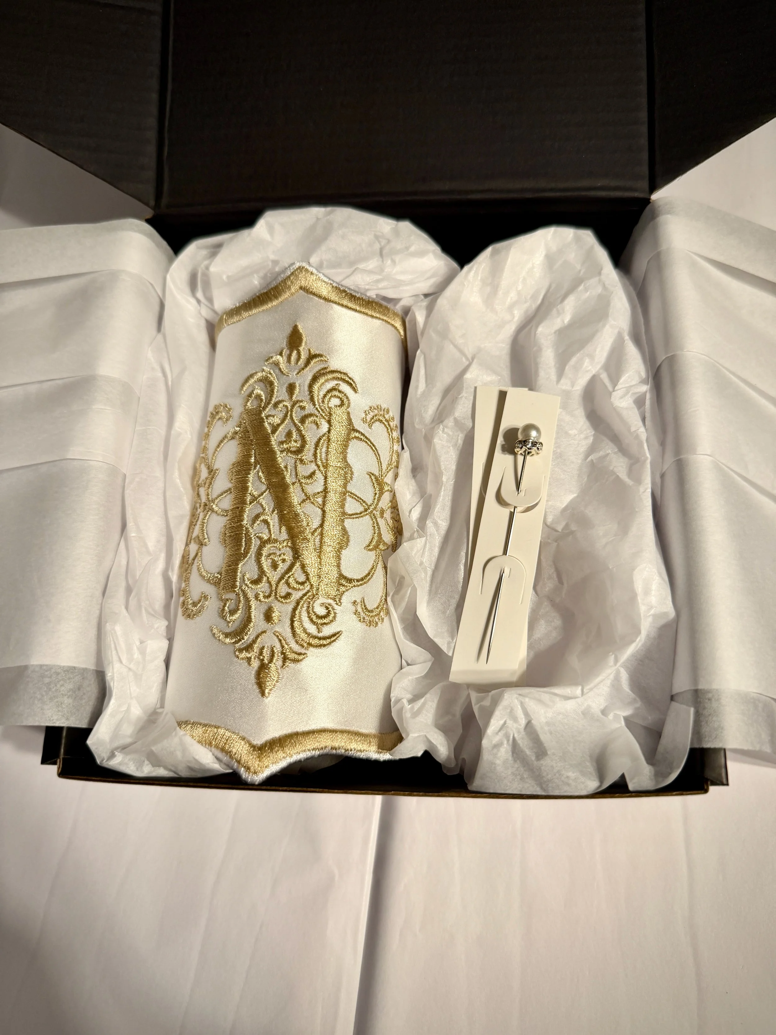 A box containing a gold and cream embroidered silk clutch purse and a pearl and rhinestone pin with a backing card.