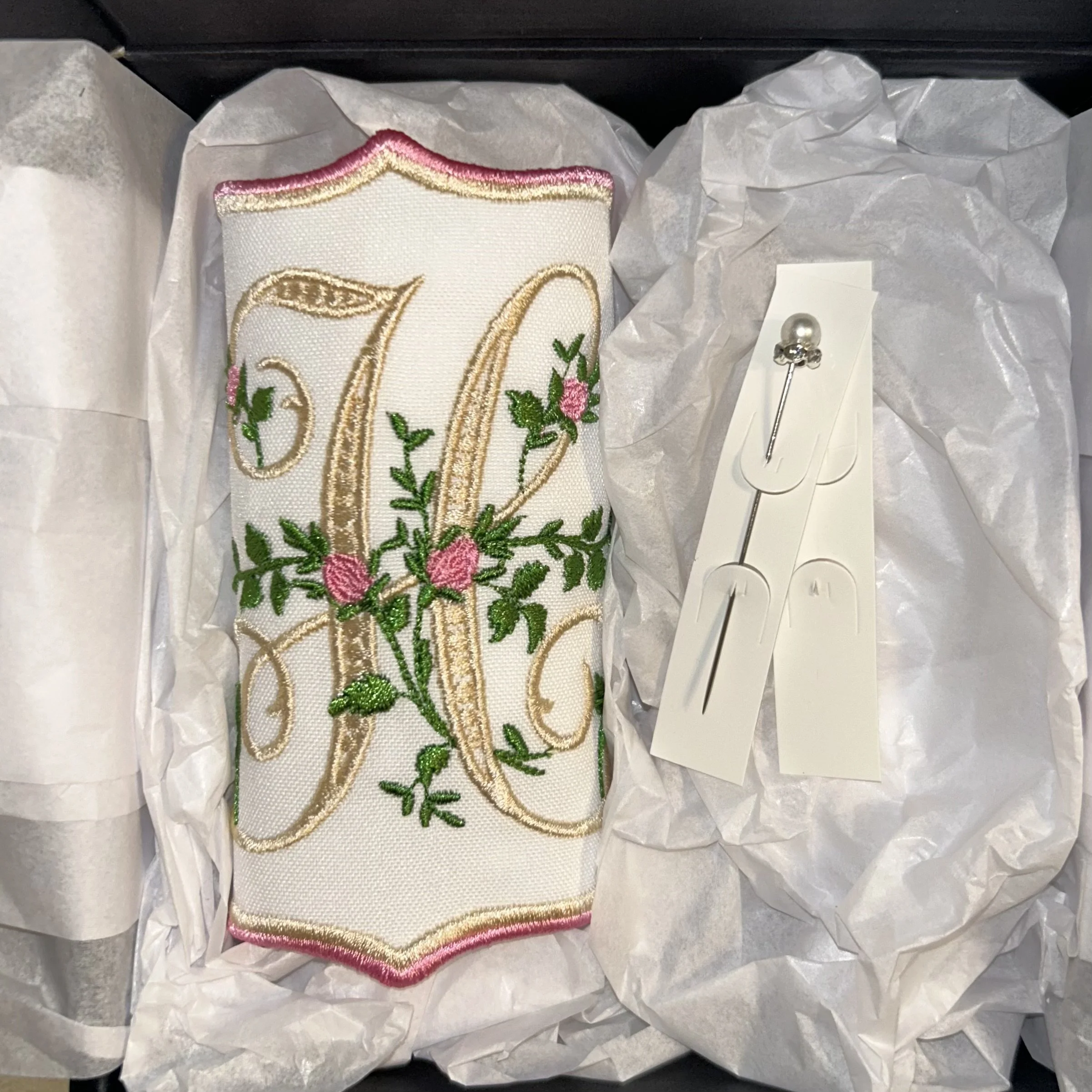 Embroidery of a letter 'D' with pink roses and green leaves, surrounded by white tissue paper.