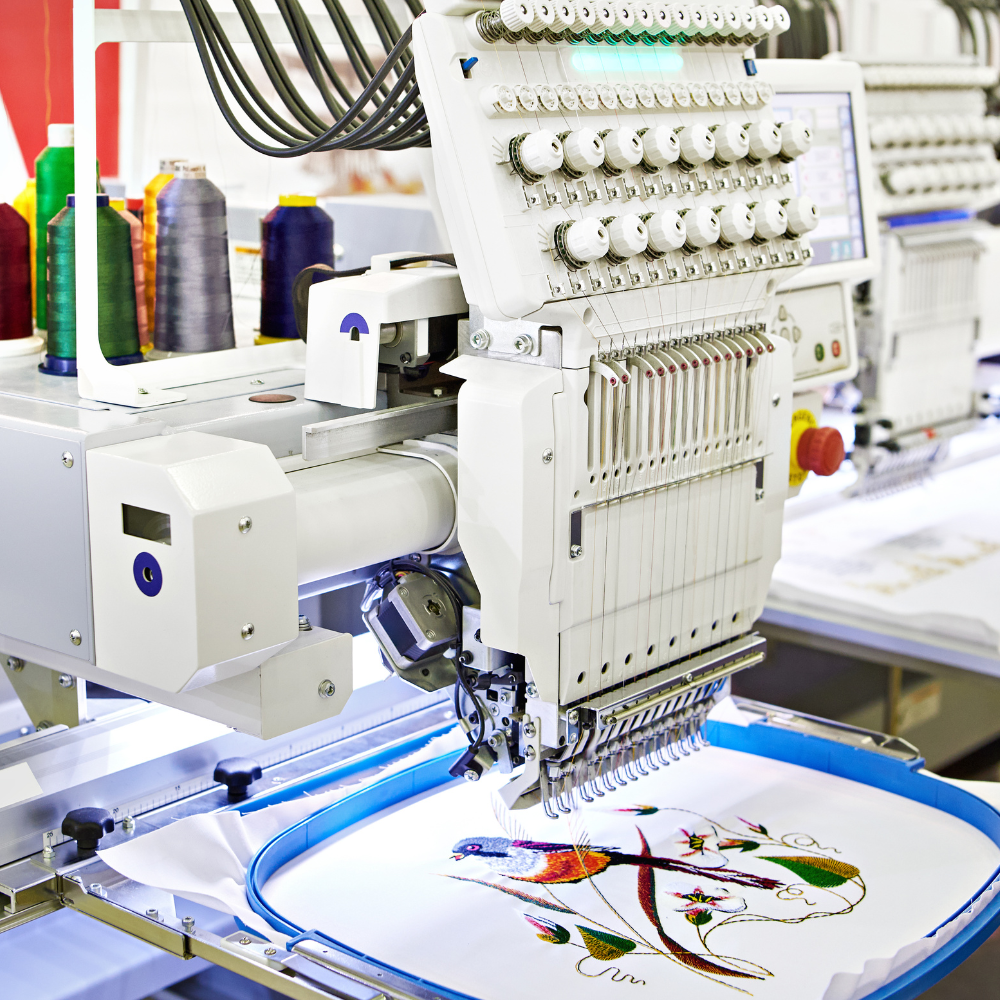 Close-up of embroidery machine stitching a colorful bird design on white fabric.