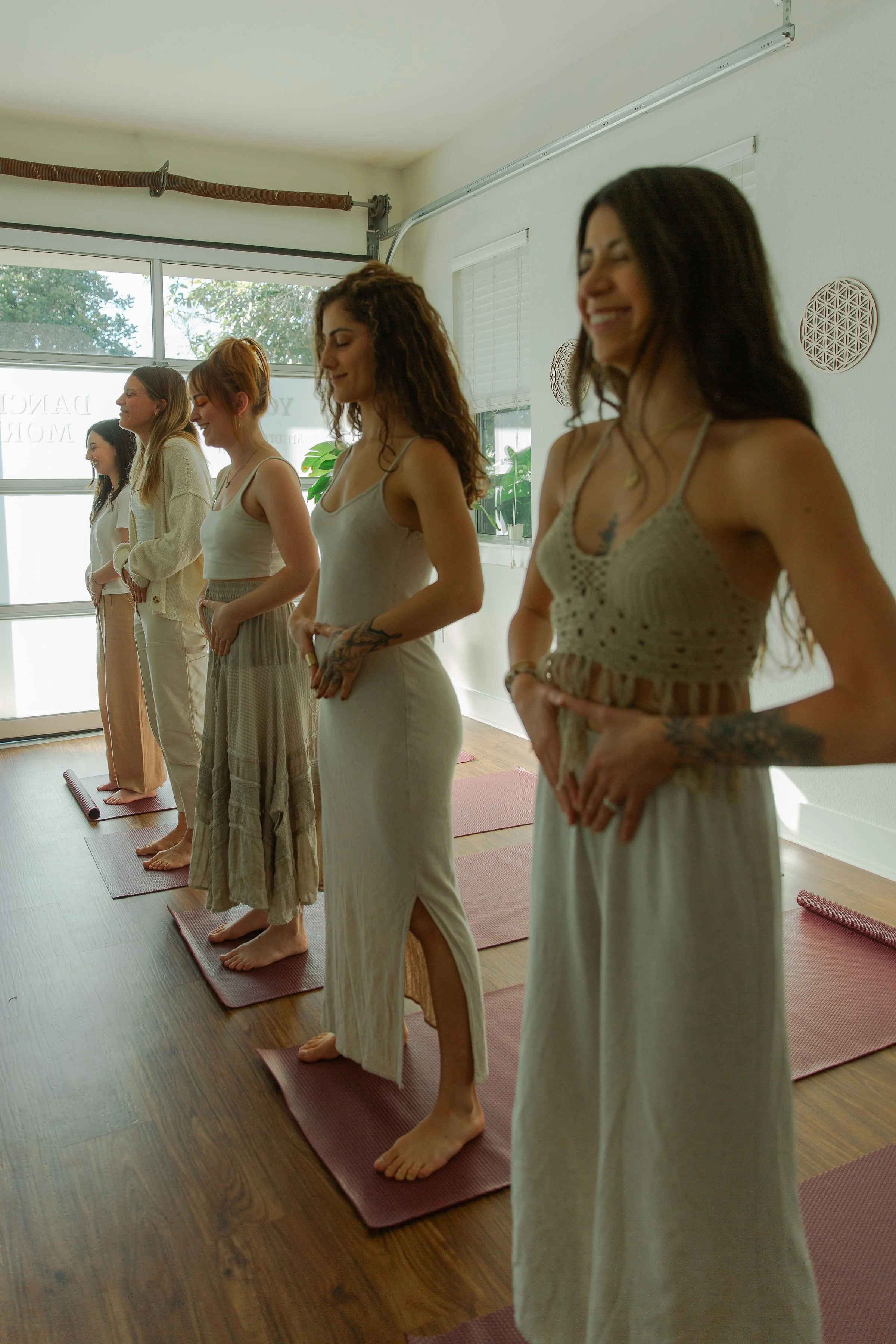 Group of people in yoga class standing on mats, practicing mindfulness in bright studio.