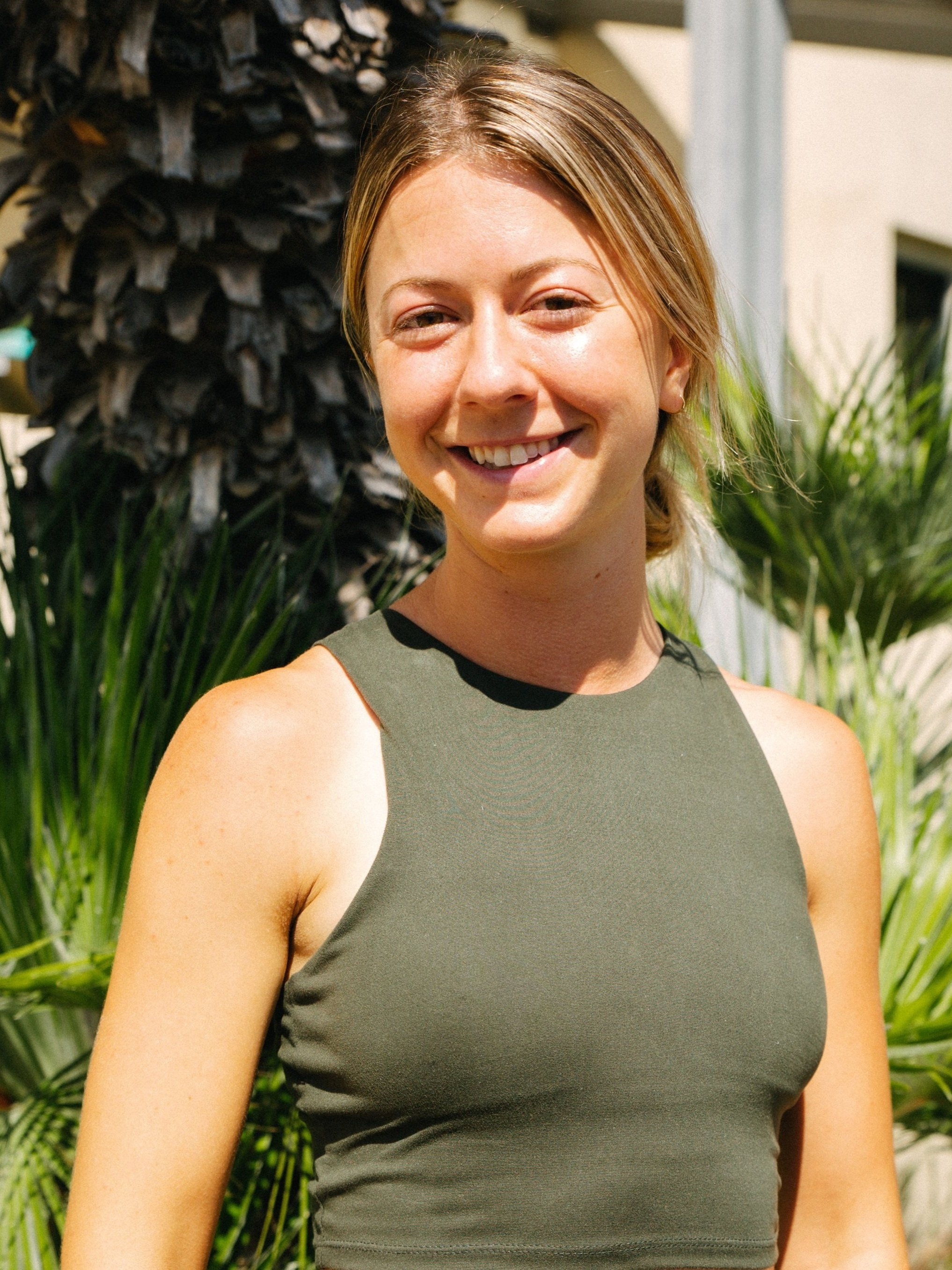 Woman in sleeveless top smiling outdoors near palm tree