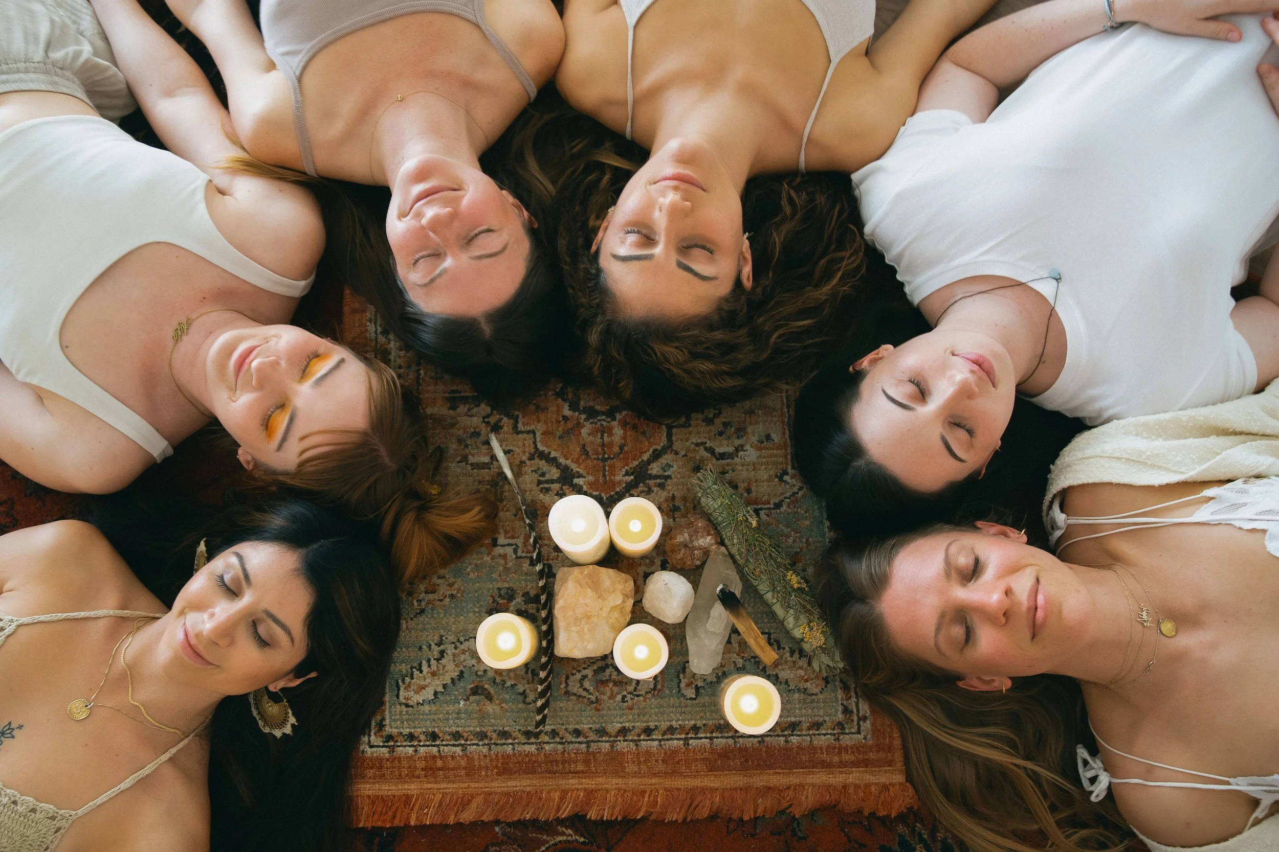 Group of women lying in a circle with heads together, symbolizing unity, community, and sacred sisterhood during a group wellness or yoga retreat.