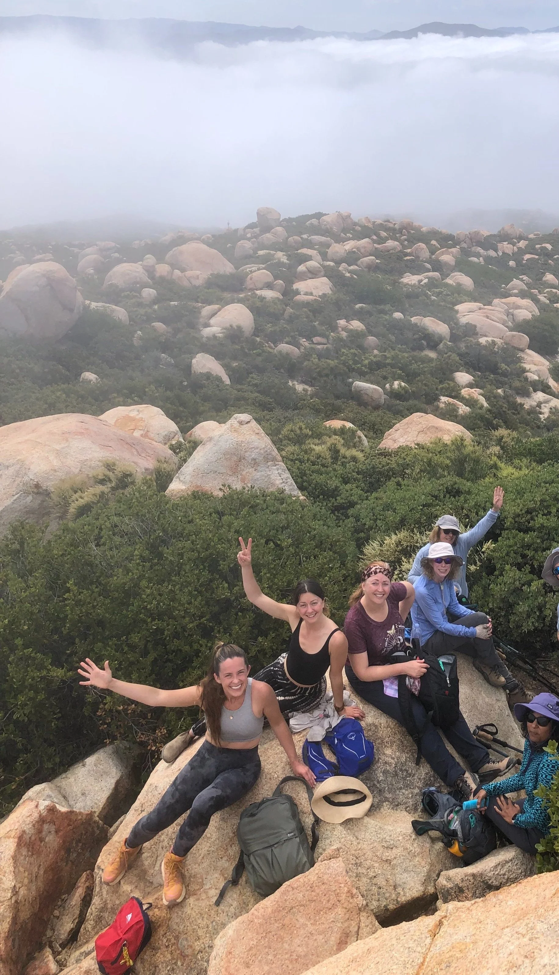 Group of hikers sitting on rocks with foggy landscape and boulders in the background.