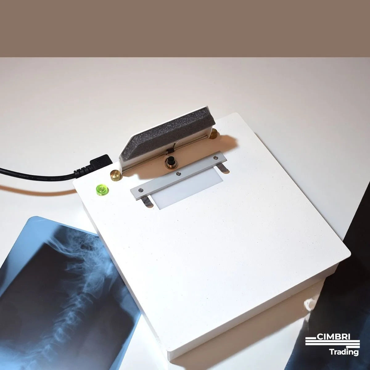 Medical X-ray scanner machine on a white table, with an X-ray image of a spinal column nearby.