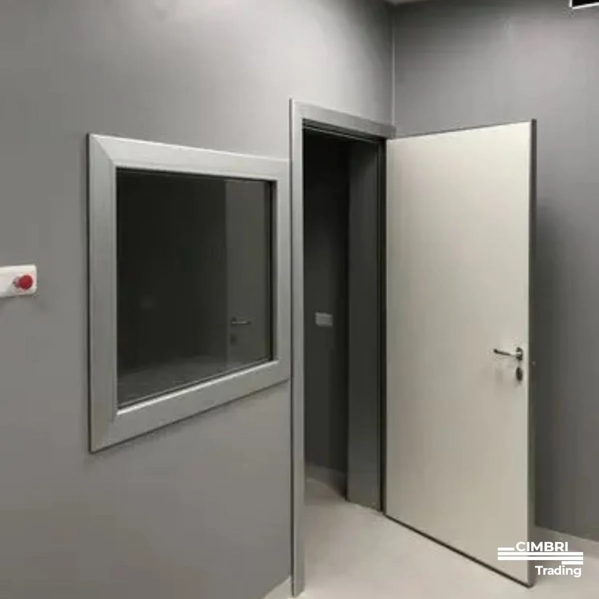 An interior room with gray walls, a circular red and white device on the wall, a window with a metallic frame, and an open door leading to a dark space.