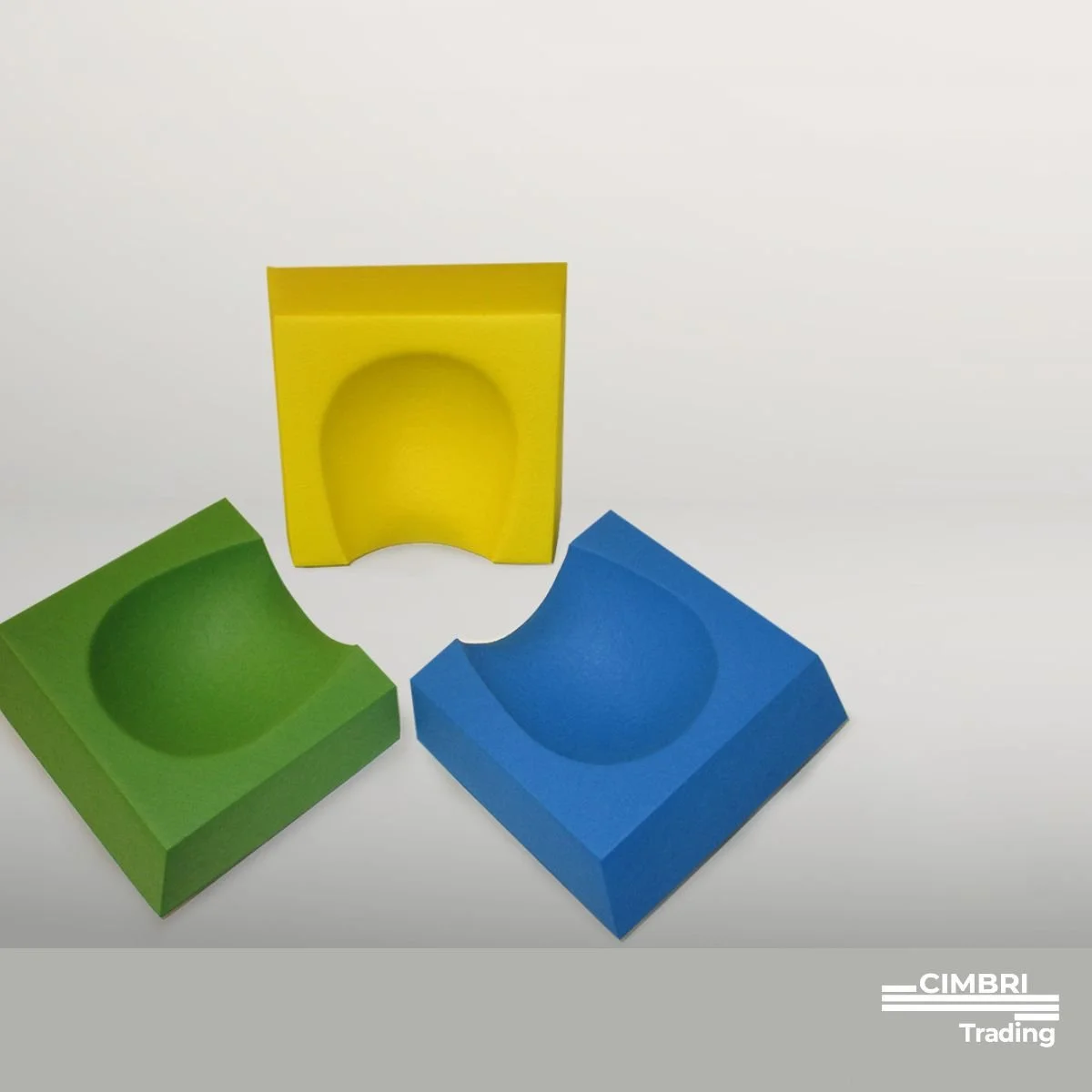 Three colorful wooden blocks with semi-spherical indentations, arranged on a white surface against a plain background. One block is yellow, one green, and one blue.