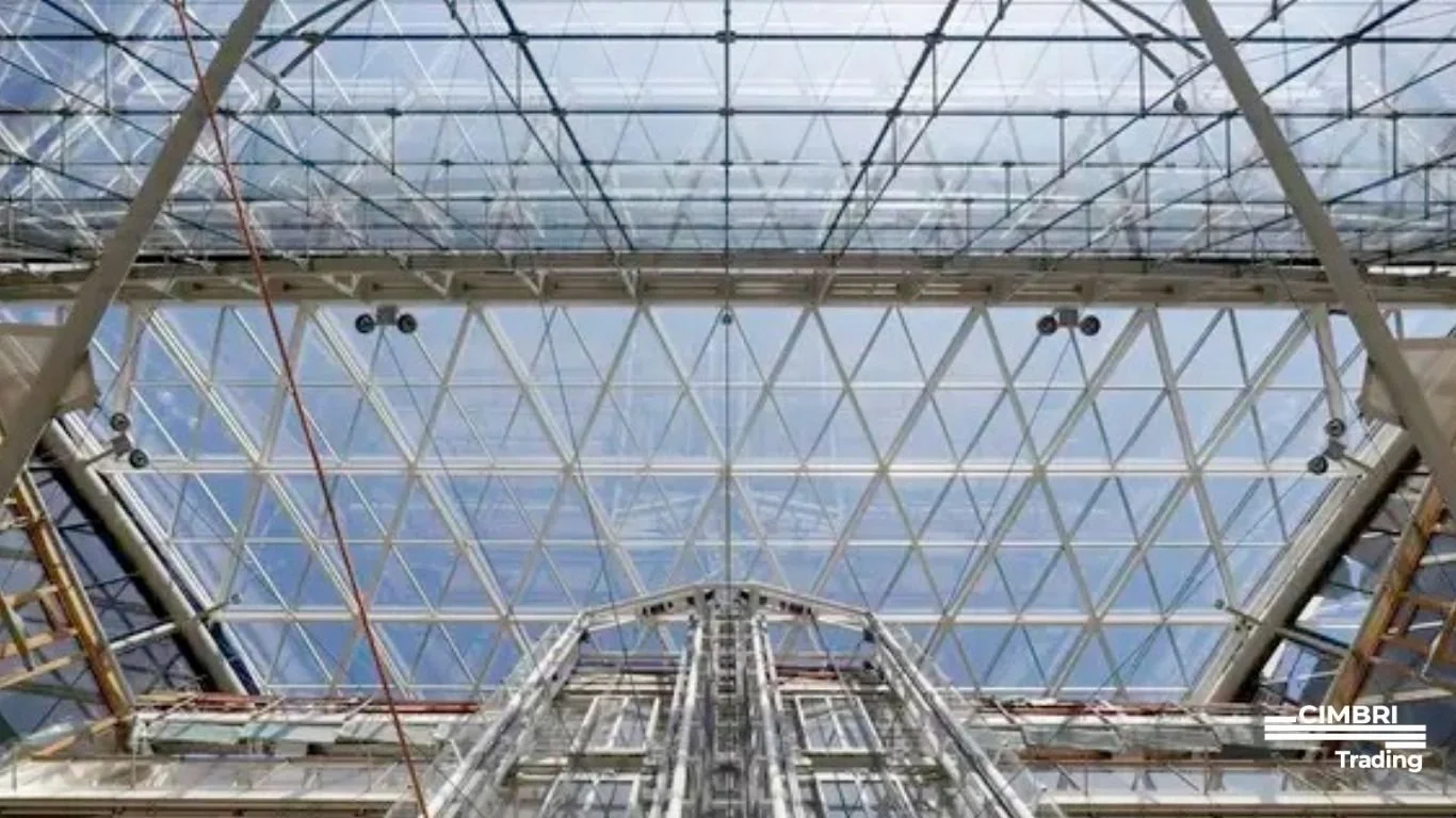 Looking up at a modern glass ceiling with a metal framework inside a building. The ceiling features a geometric pattern with triangular glass panels.