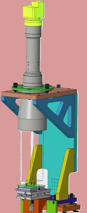 A vertical industrial machine with a yellow top, gray middle section, mounted on a colorful support structure with various components, set against a pink background.