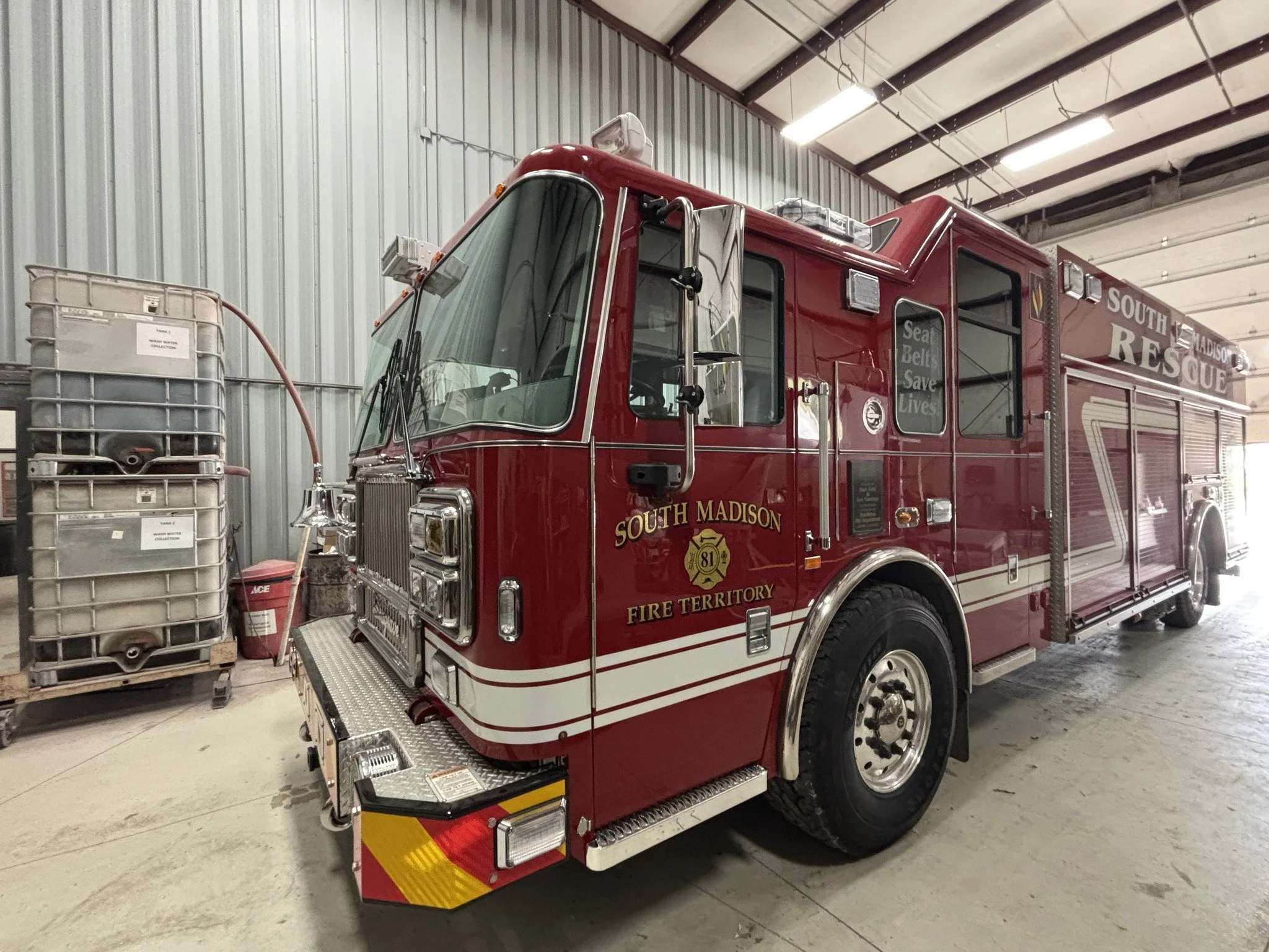Red fire rescue truck inside a warehouse, with capacity and safety equipment visible on the truck and stacked water tanks nearby.