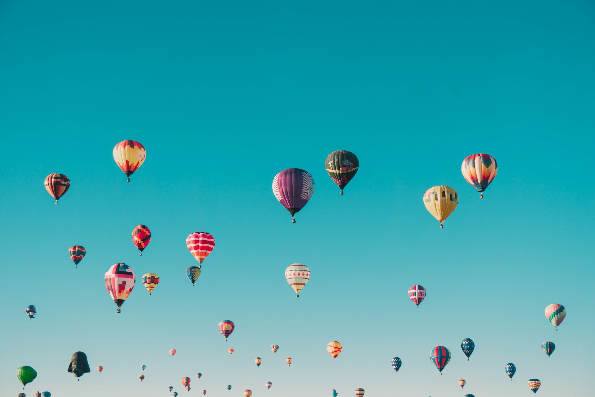 Numerous colorful hot air balloons floating in a clear blue sky during daytime.