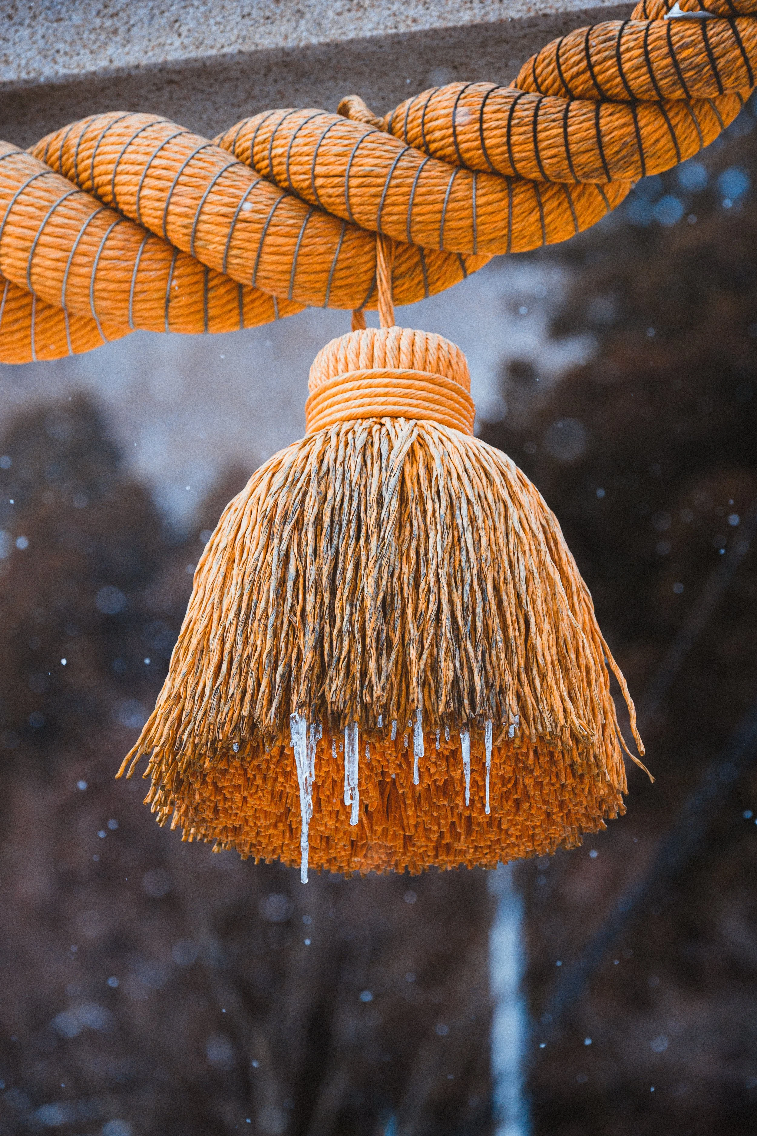 A close-up of an orange, woven-cloth hanging lamp with icicles hanging from the bottom, with a dark background and blurred bokeh lights.