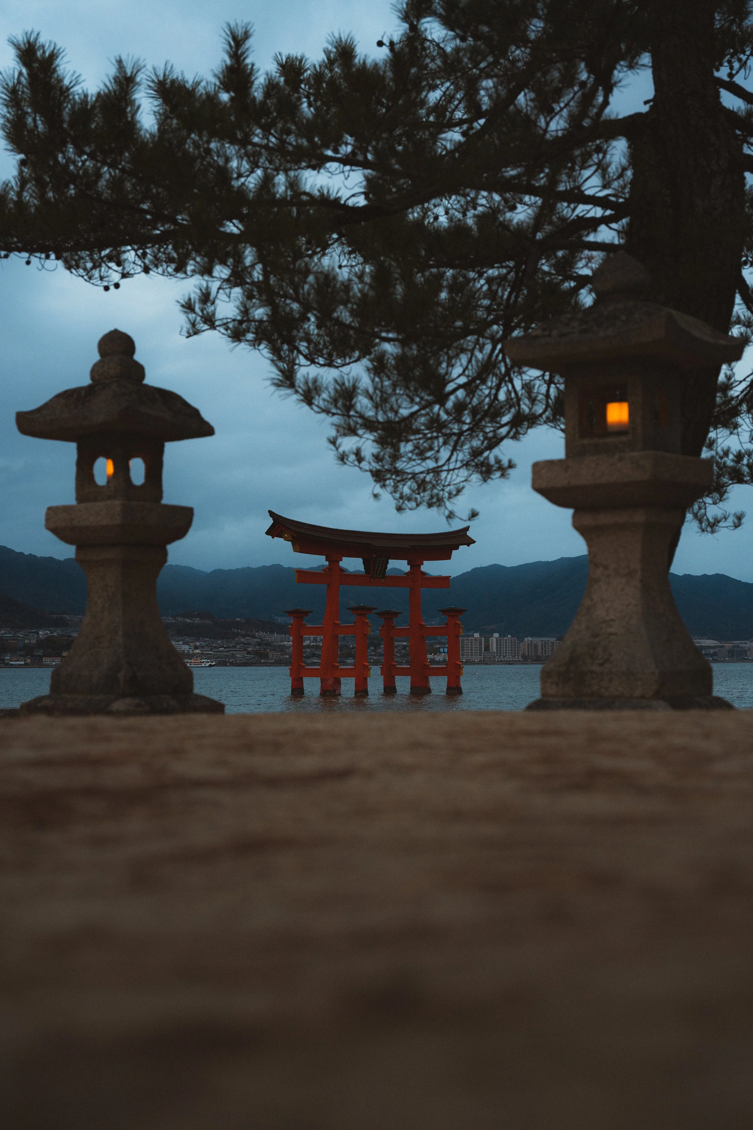 Traditional Japanese stone lanterns in the foreground with a red torii gate and mountain in the background during dusk.