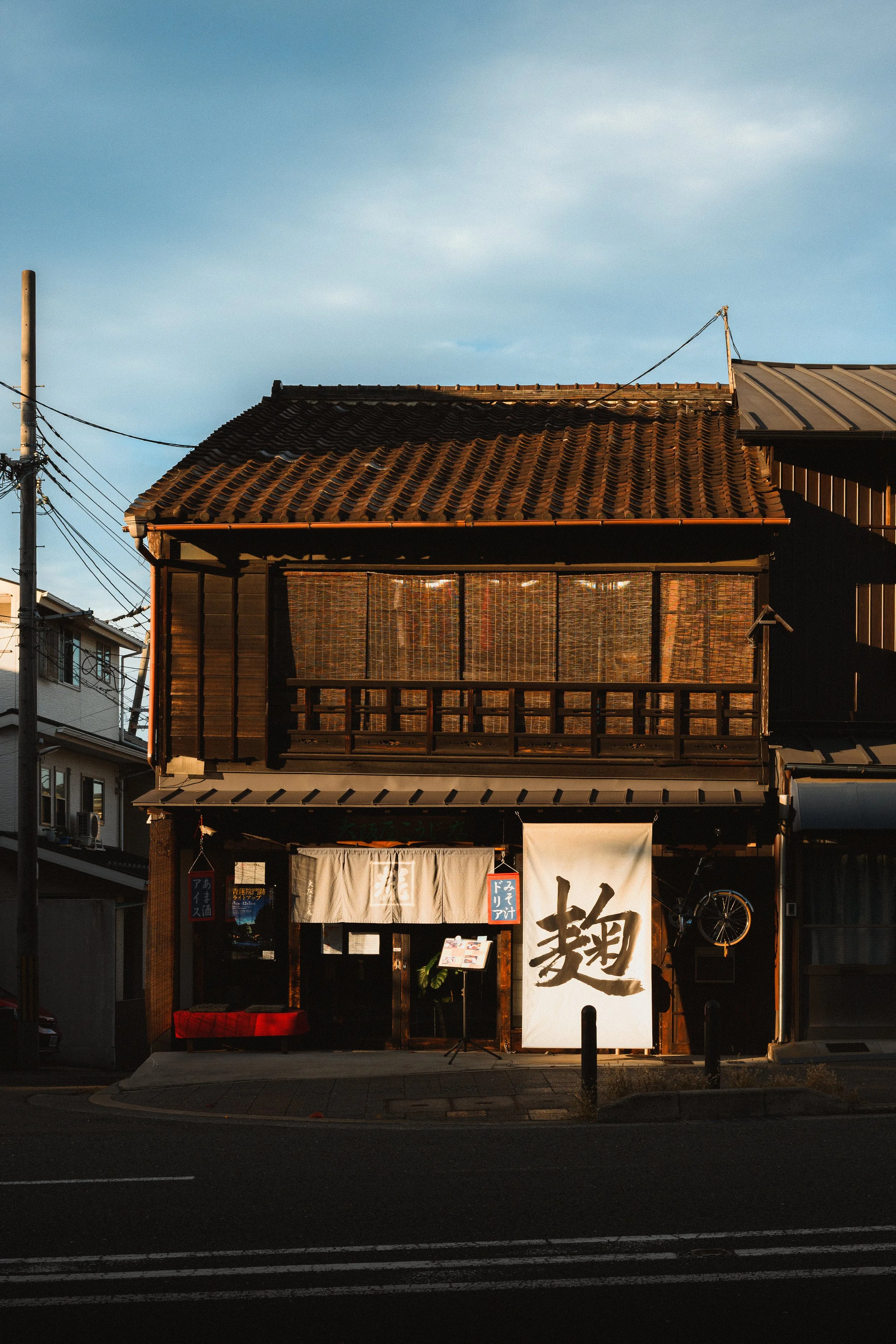 A traditional Japanese restaurant with a tiled roof, wooden exterior, and Japanese signage, illuminated by warm evening light.