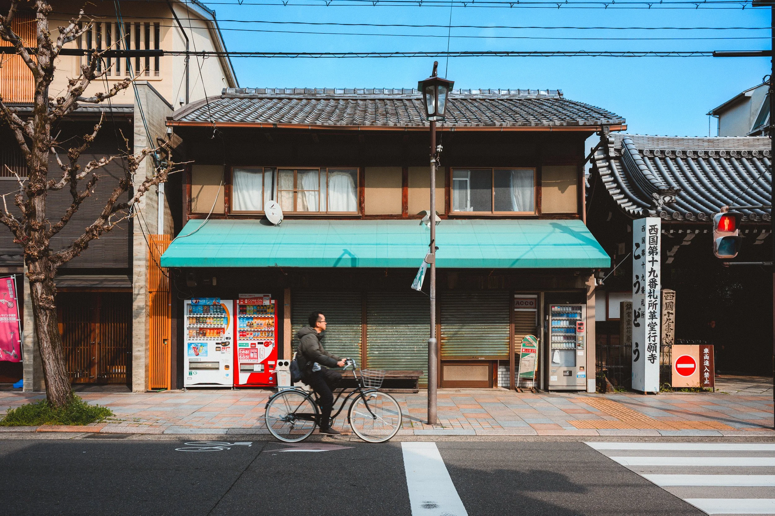 A person riding a bicycle past storefronts with vending machines on a city street, with a utility pole and power lines overhead.