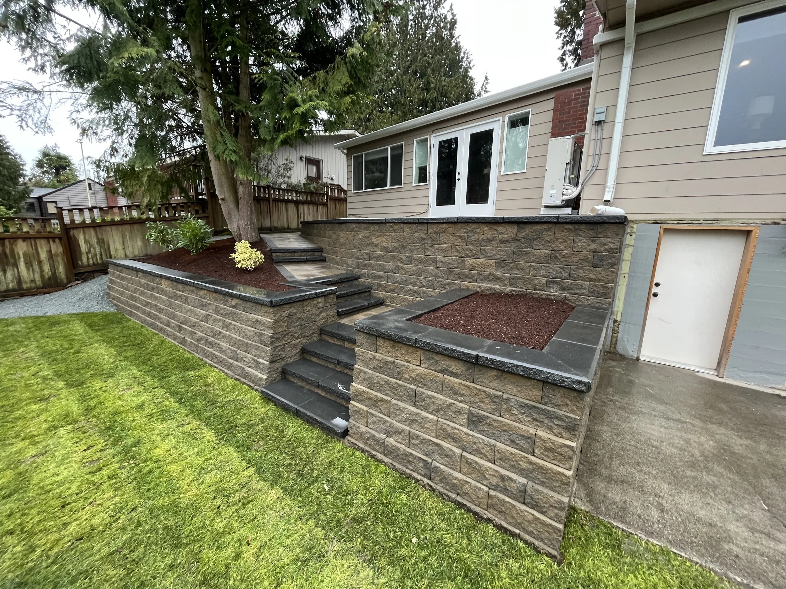 Backyard with a tree, a wooden fence, a stone and concrete staircase, and a house with sliding glass doors.