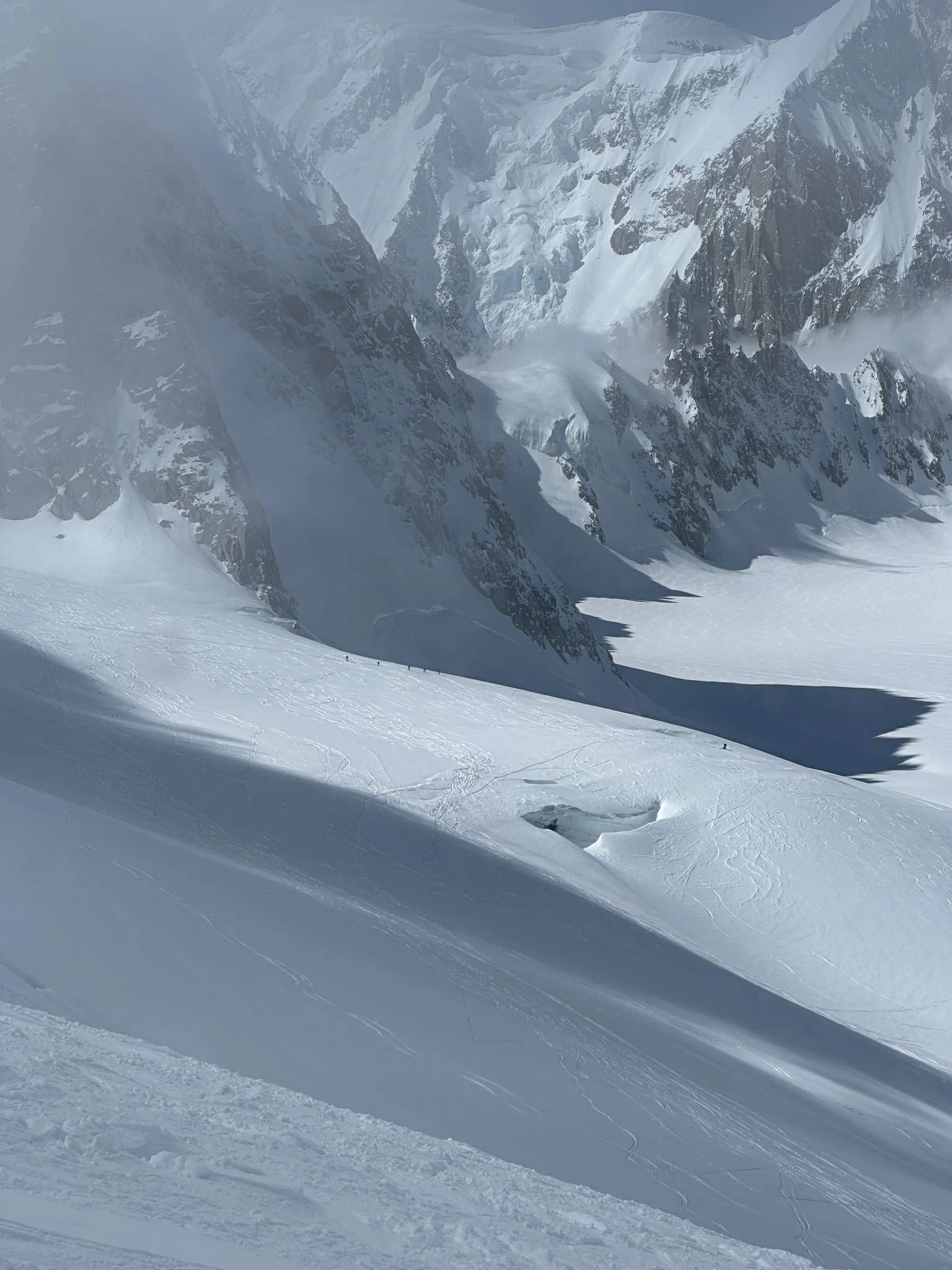Snow-covered mountain landscape with steep, jagged peaks and a snowfield below, showing some ski tracks.