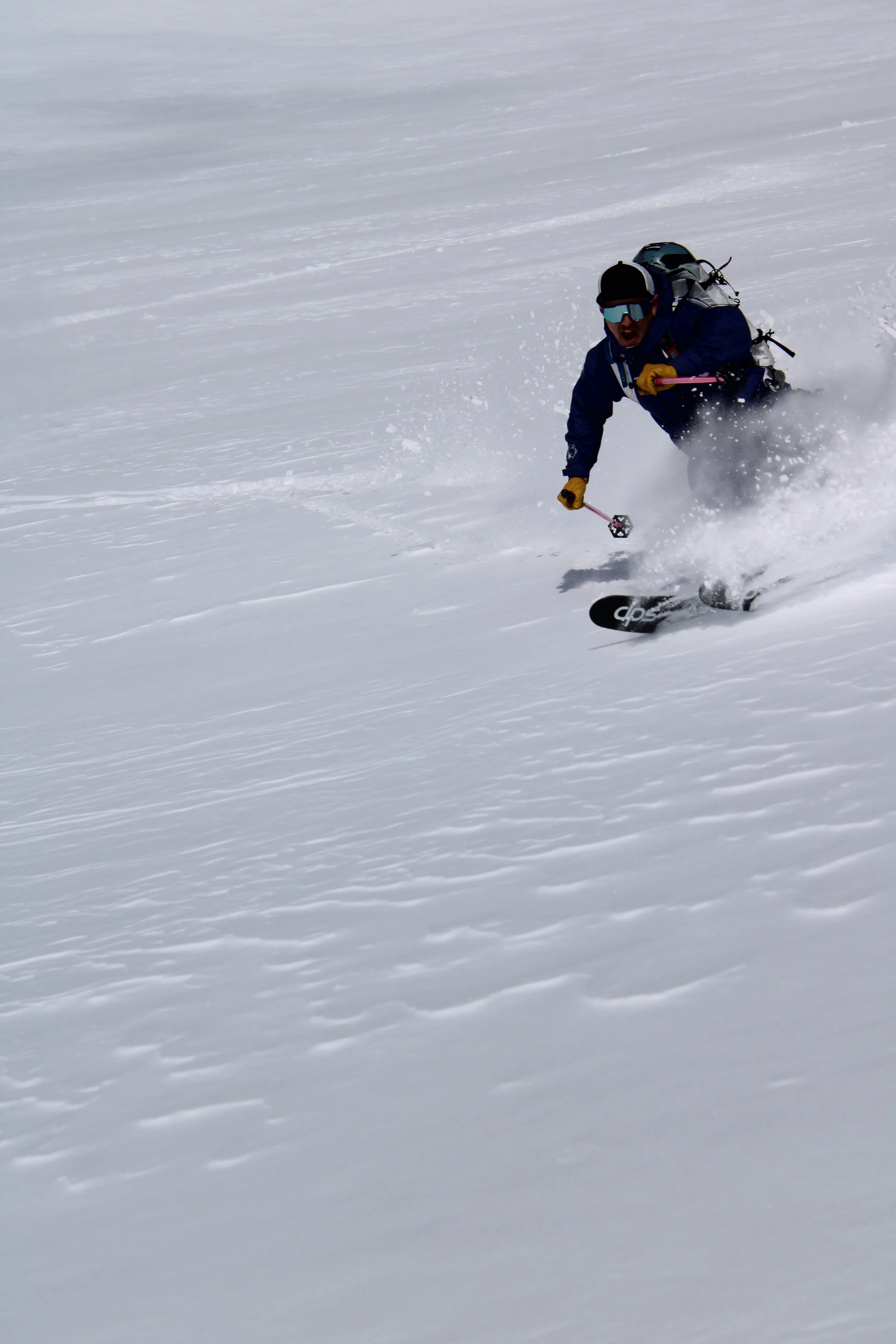 A person wearing a blue jacket, yellow gloves, sunglasses, and a helmet skiing on a snow-covered slope.