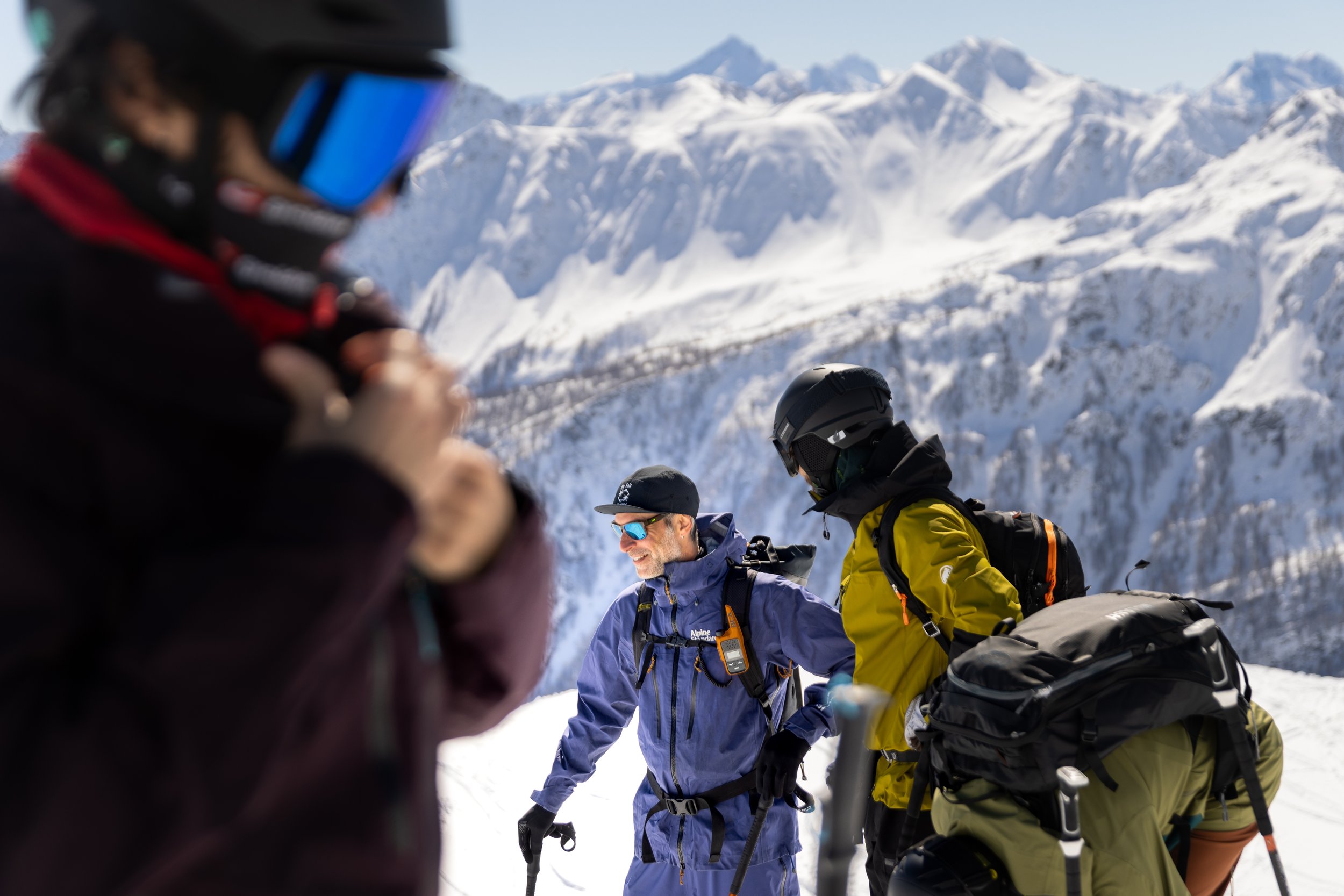 Group of people snowboarding in snowy mountains, wearing winter gear and helmets, with icy peaks in the background.