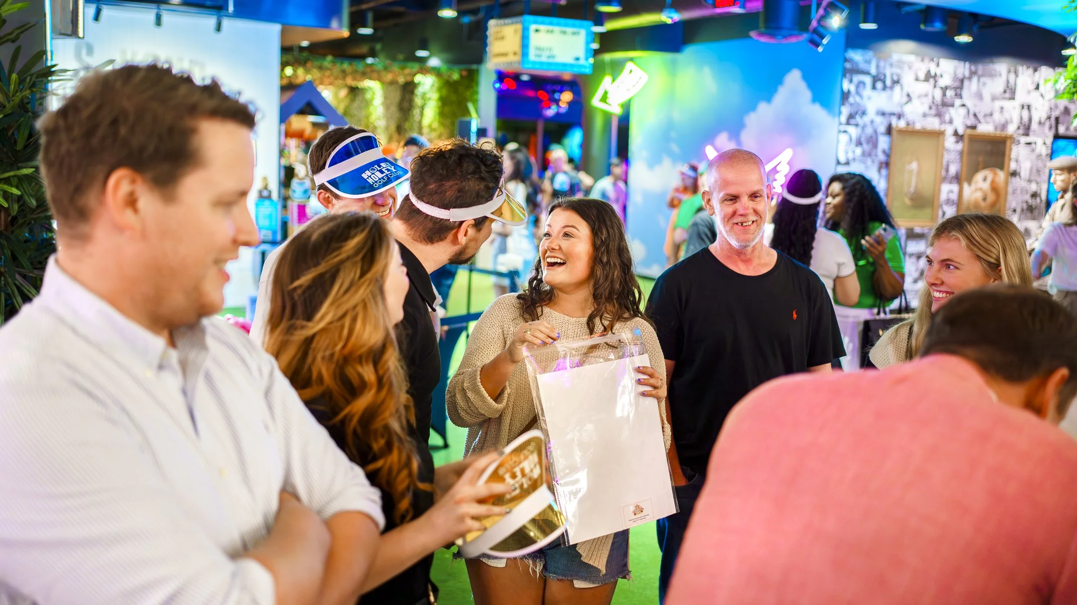 Group of people smiling and chatting at an indoor event with colorful neon lights and wall decorations.