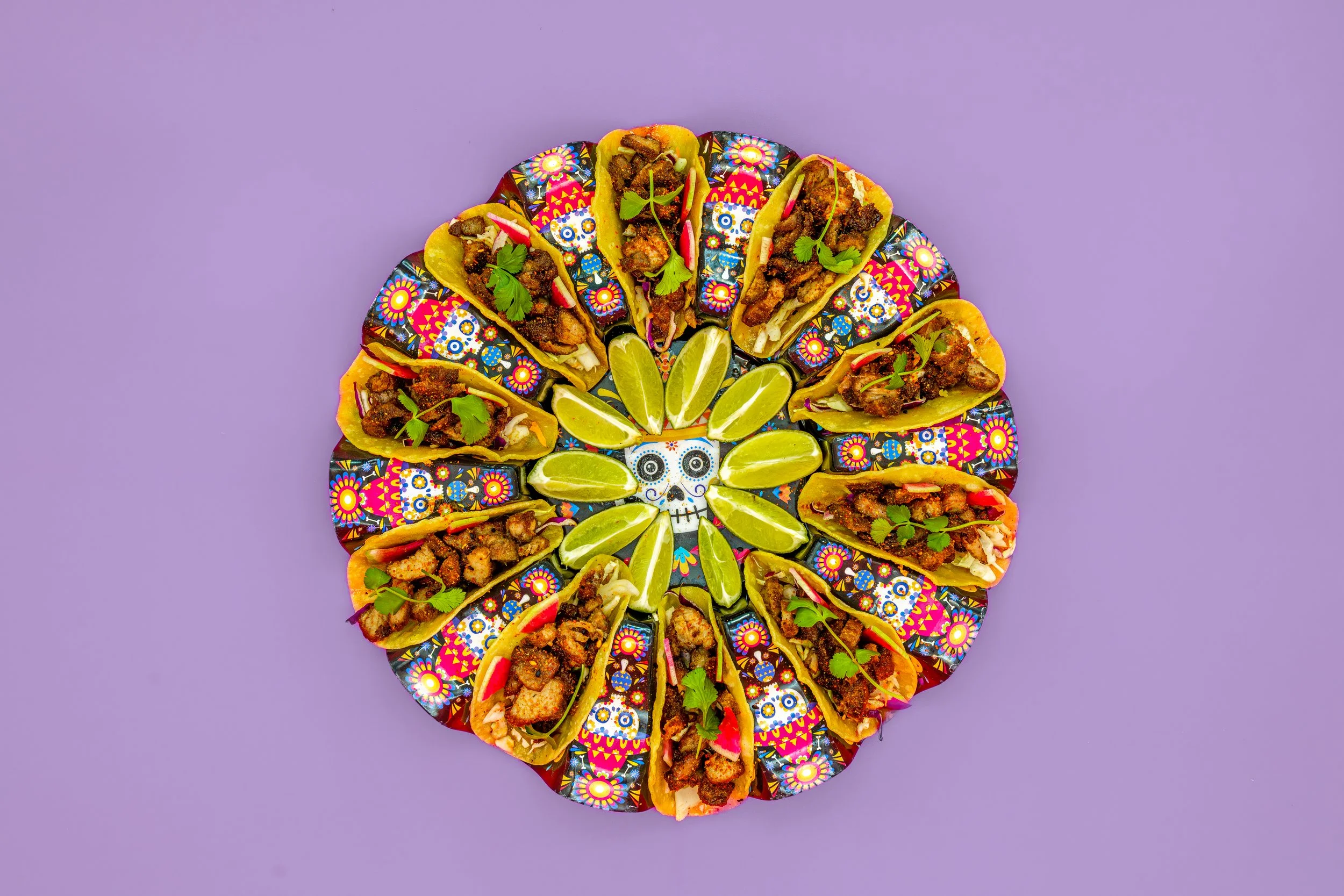 A circular arrangement of colorful tacos decorated with cilantro and lime wedges on a purple background.