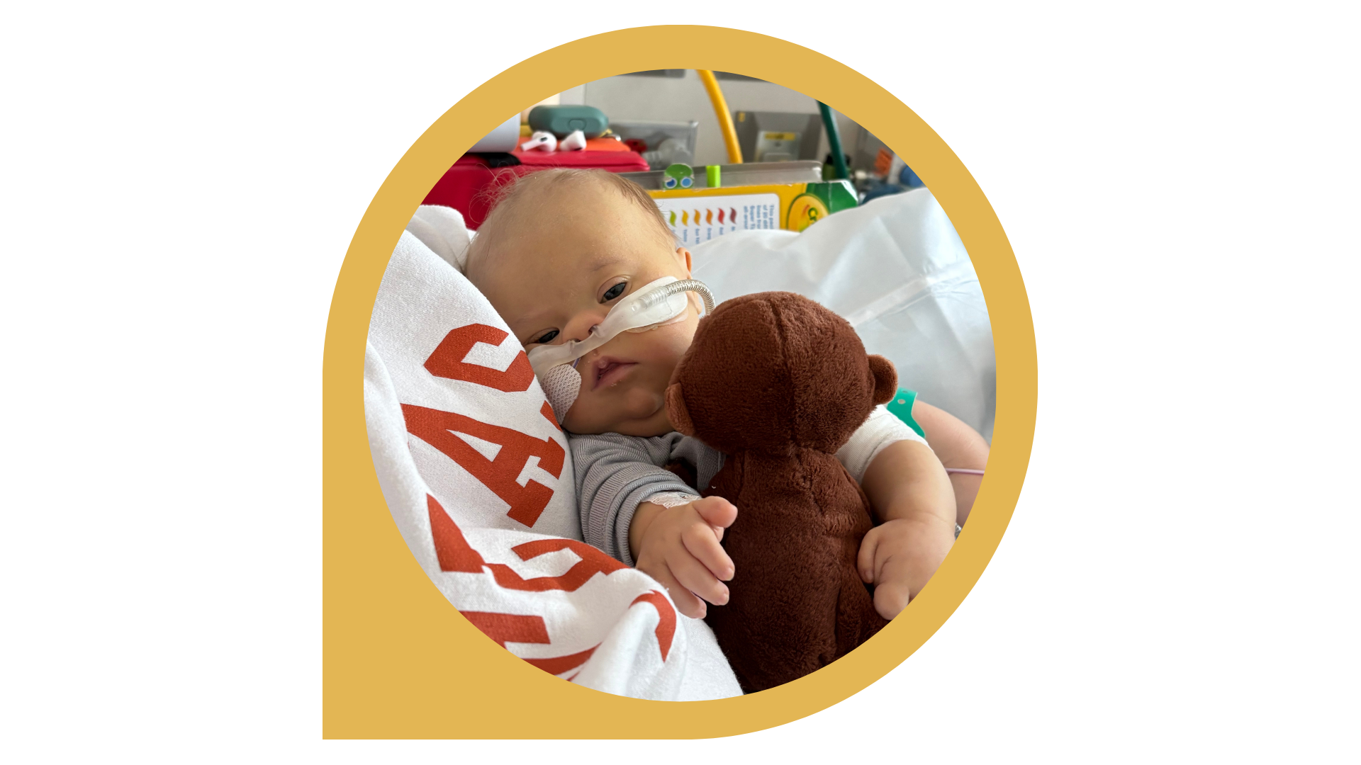 A young child in a hospital bed, wearing a nasal cannula for oxygen, holding a brown teddy bear.
