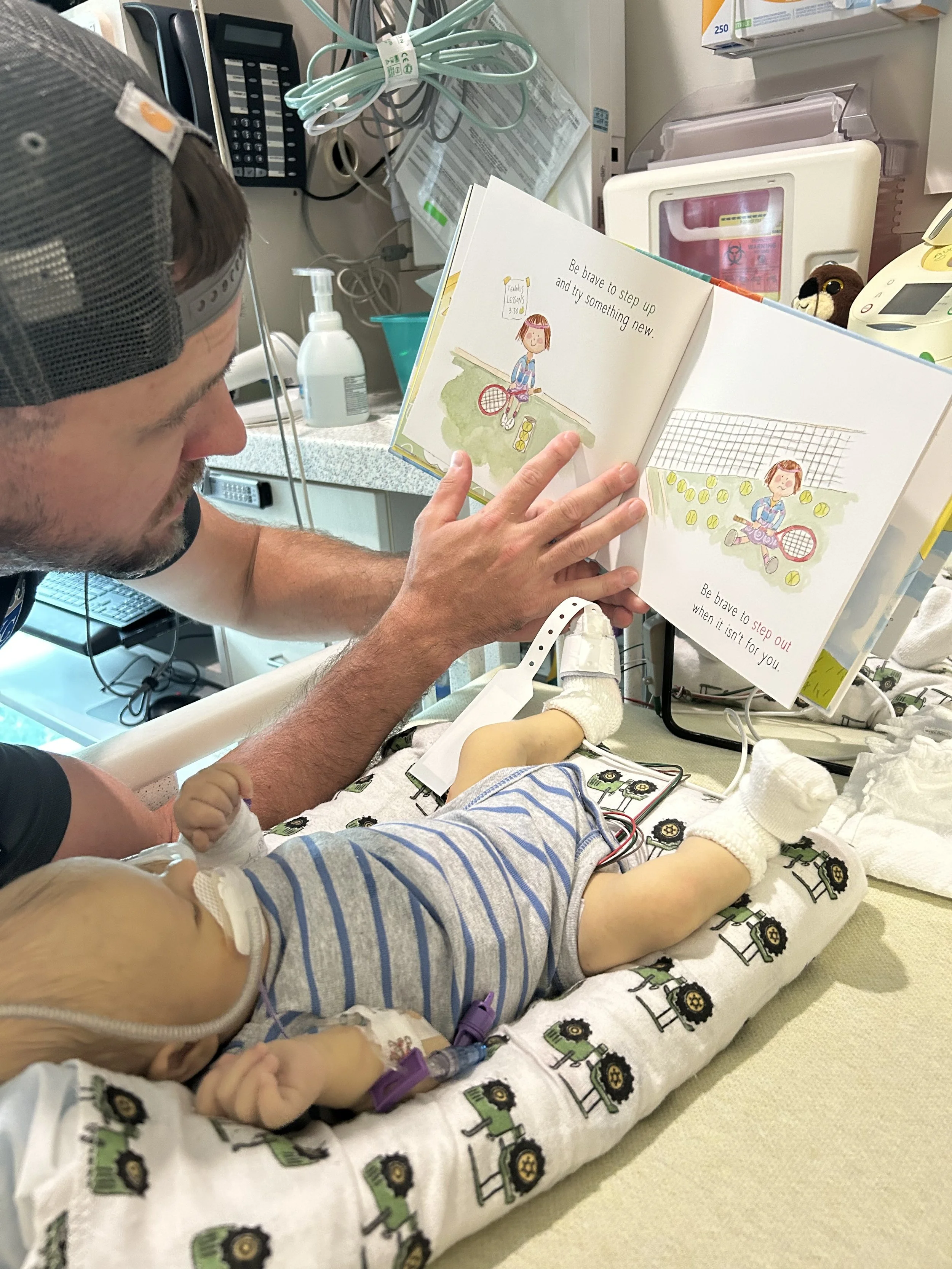 A person with a cap reads a children's picture book to a child in a hospital bed. The book features illustrations of a girl playing tennis with text encouraging bravery and trying new things.
