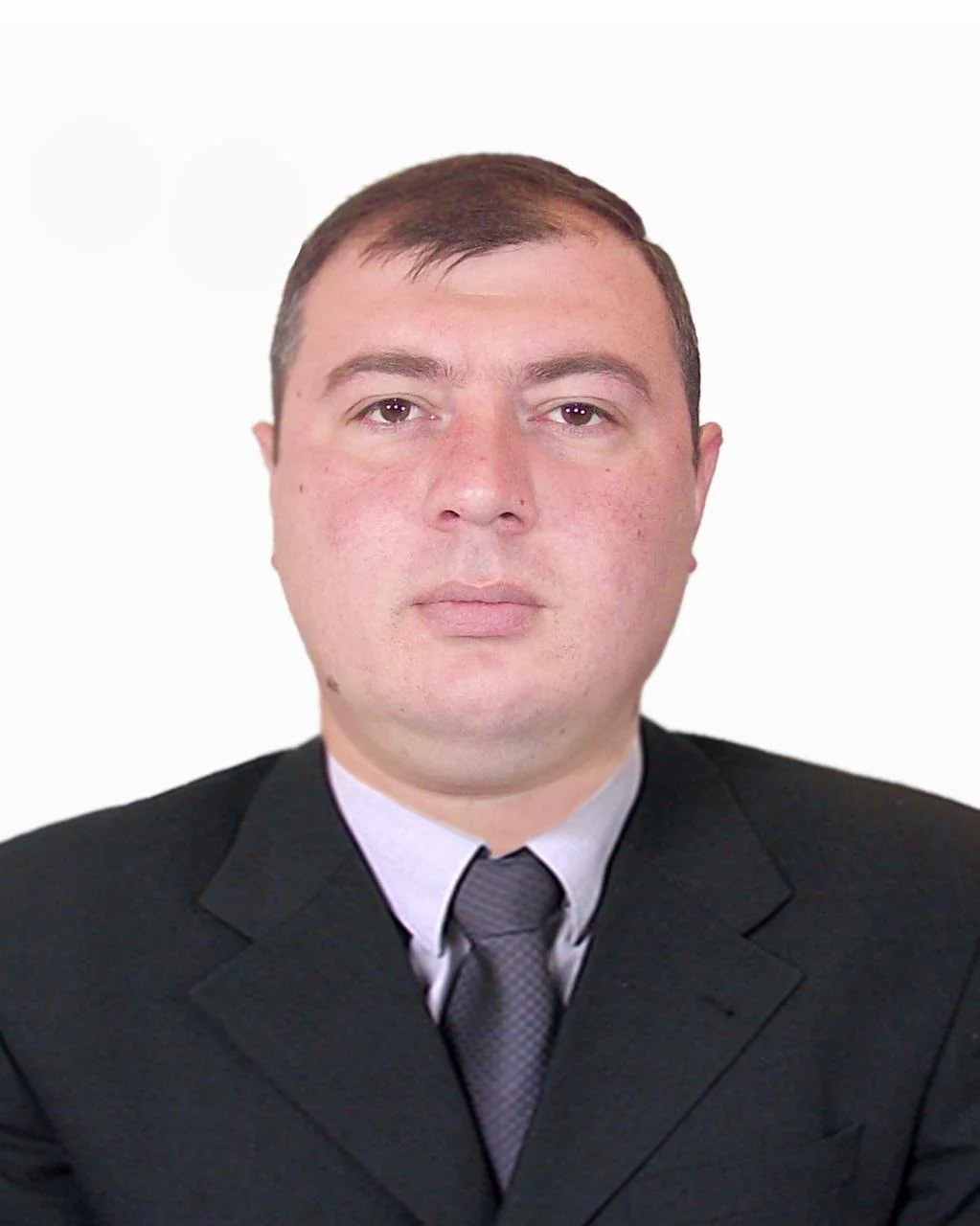 Portrait of a man in a black suit with a white shirt and gray tie, against a plain white background.