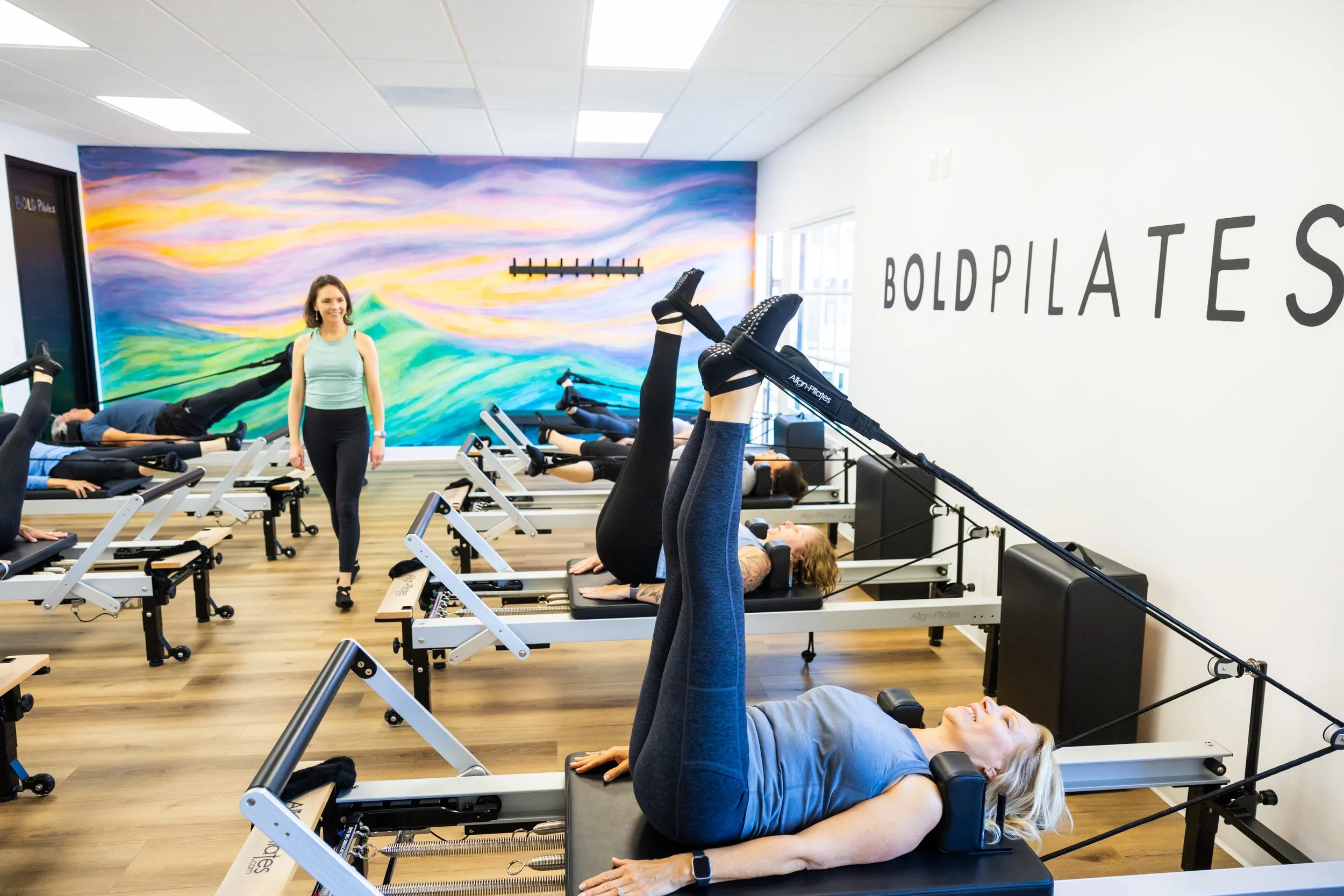 Women exercising on Pilates reformer machines at BOLD Pilates with a colorful wall mural.