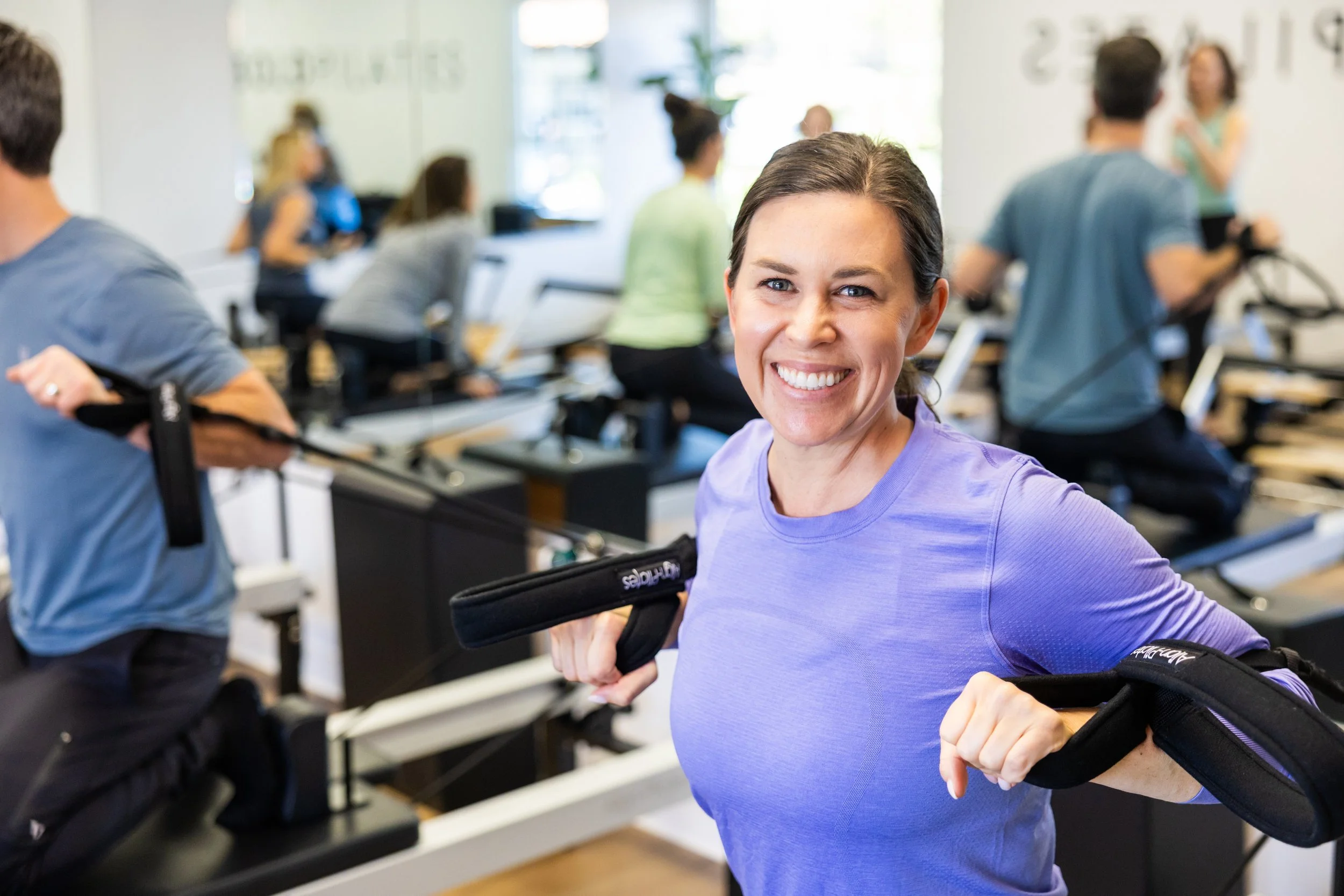 Woman smiling and exercising at BOLD Pilates Encinitas with other people working out in the background.
