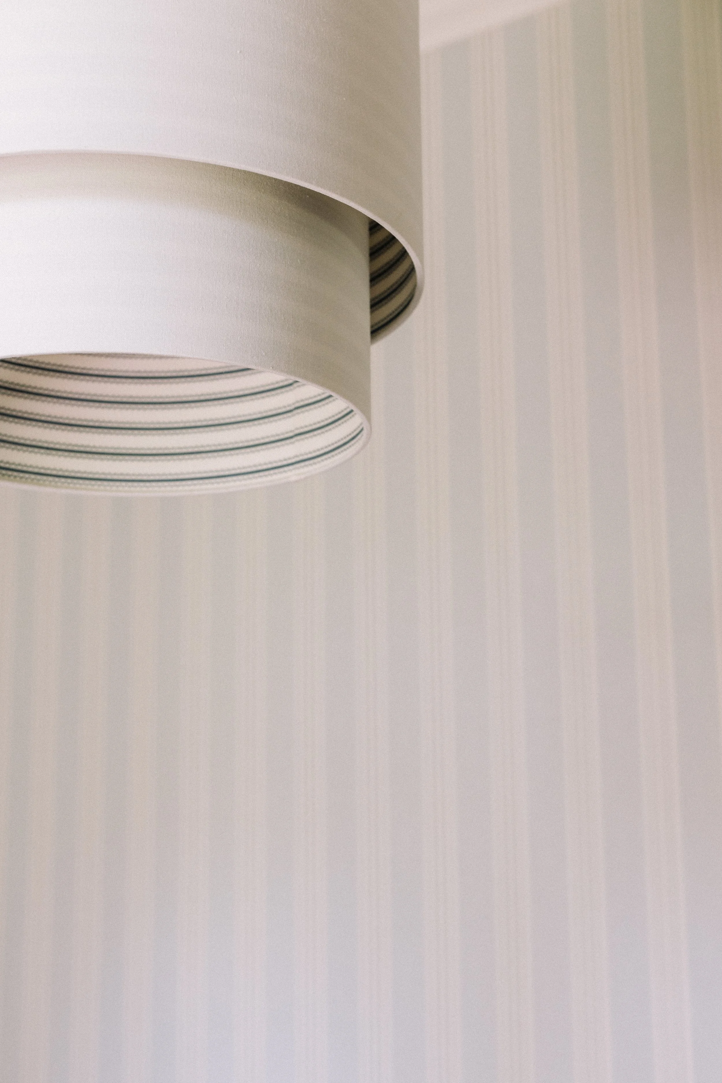 Close-up of a white lampshade with striped inner lining against a light-colored wall.